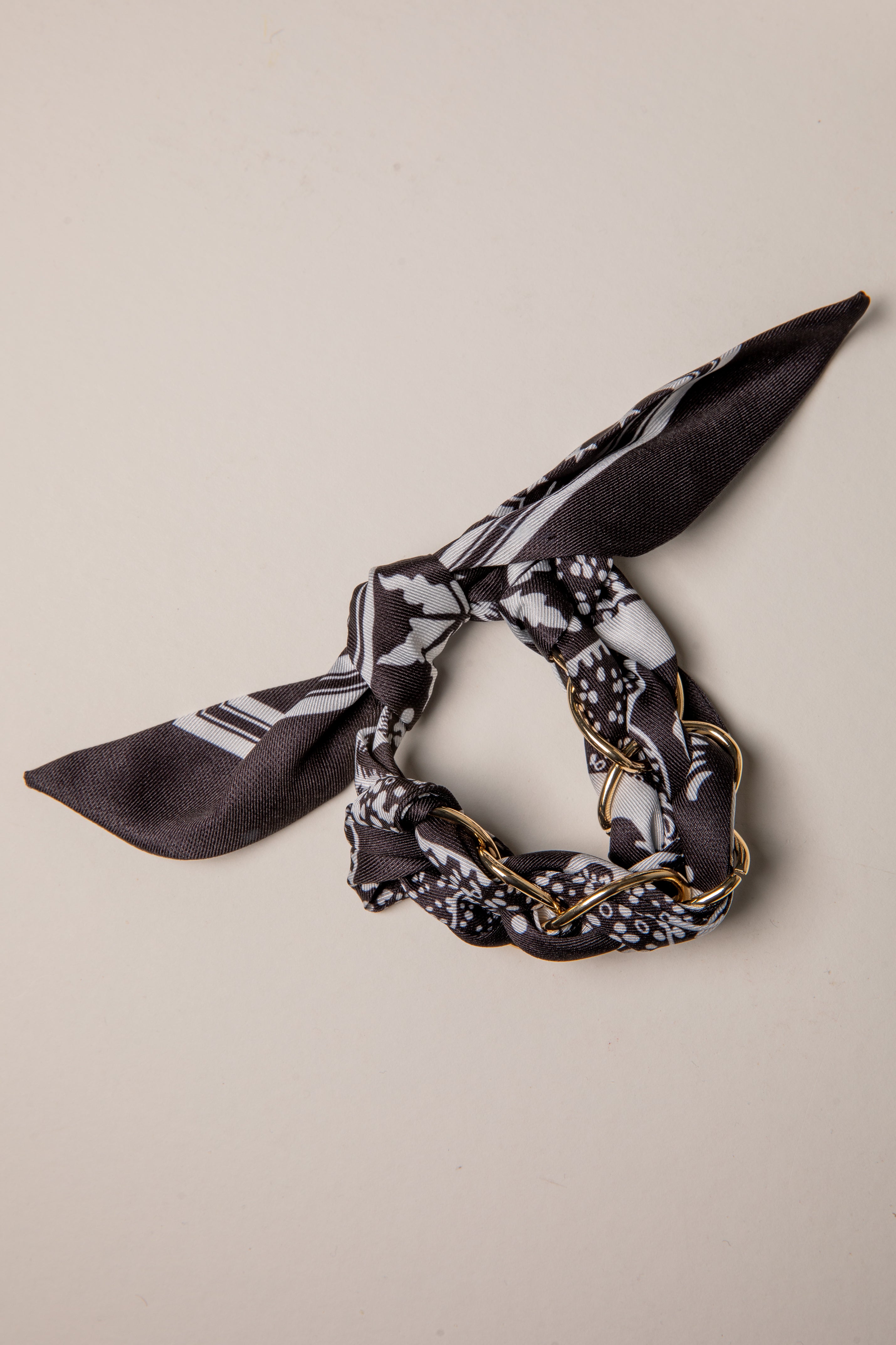 Black and white patterned scarf with gold chain on a beige background