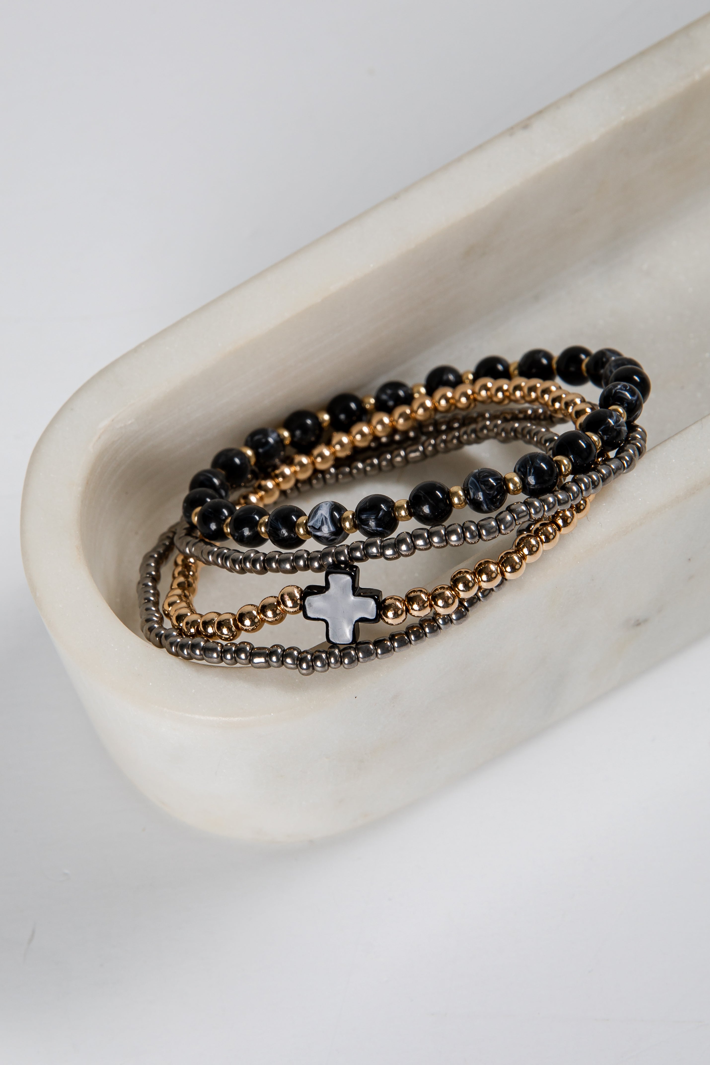 Set of three beaded bracelets with a cross charm on a white dish.