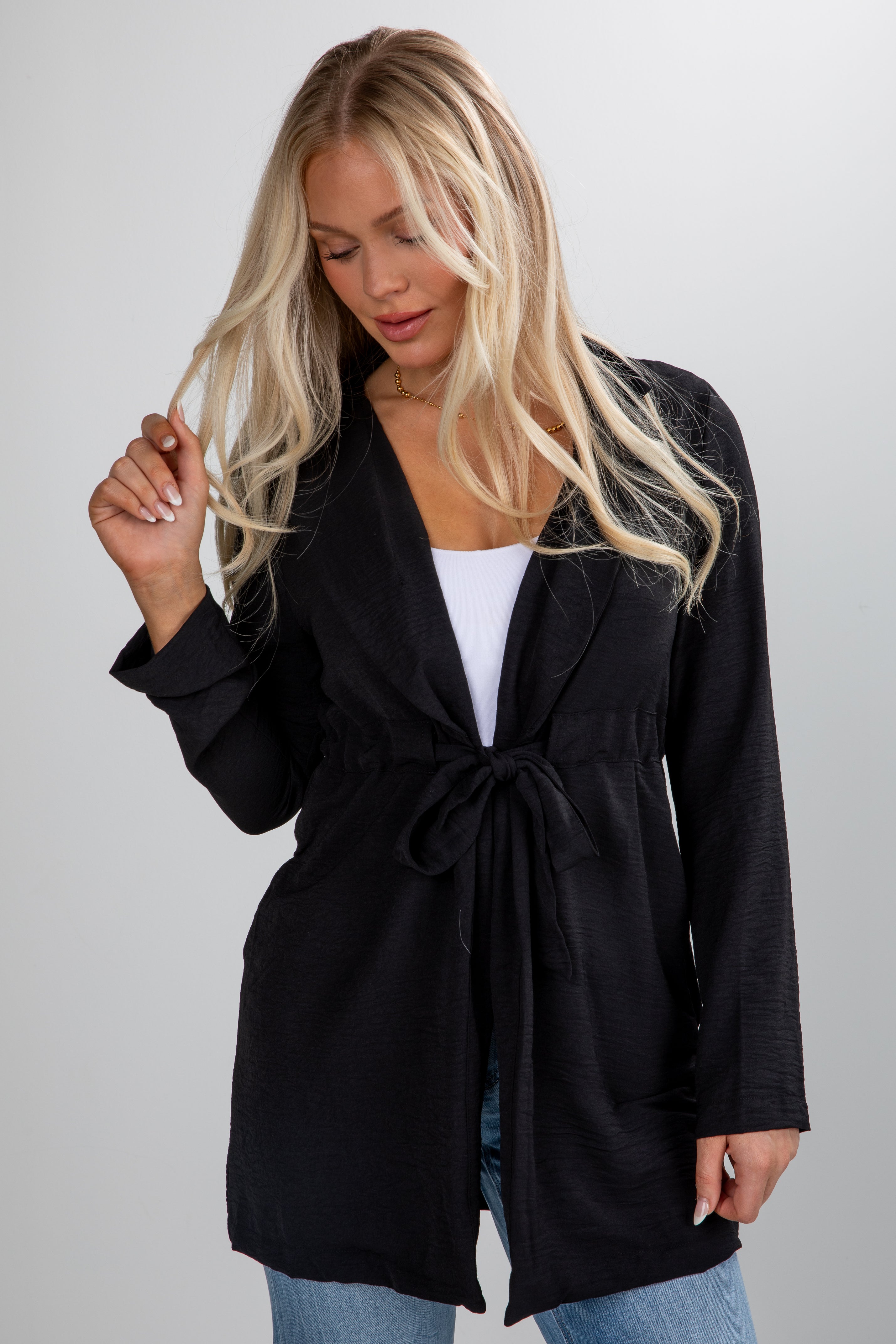 Woman wearing a black cardigan over a white top and blue jeans on a gray background