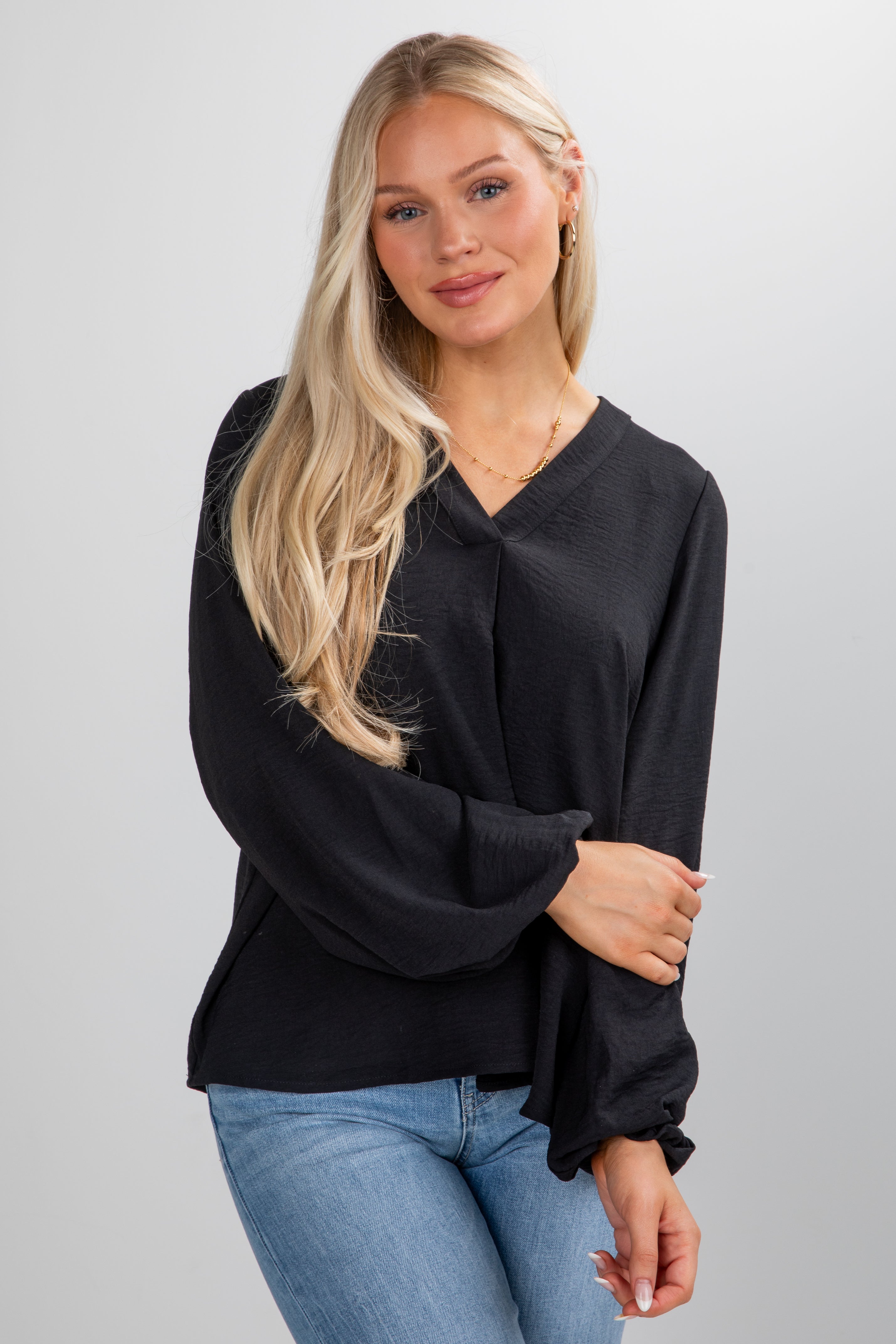 Woman wearing a black blouse and blue jeans against a plain background