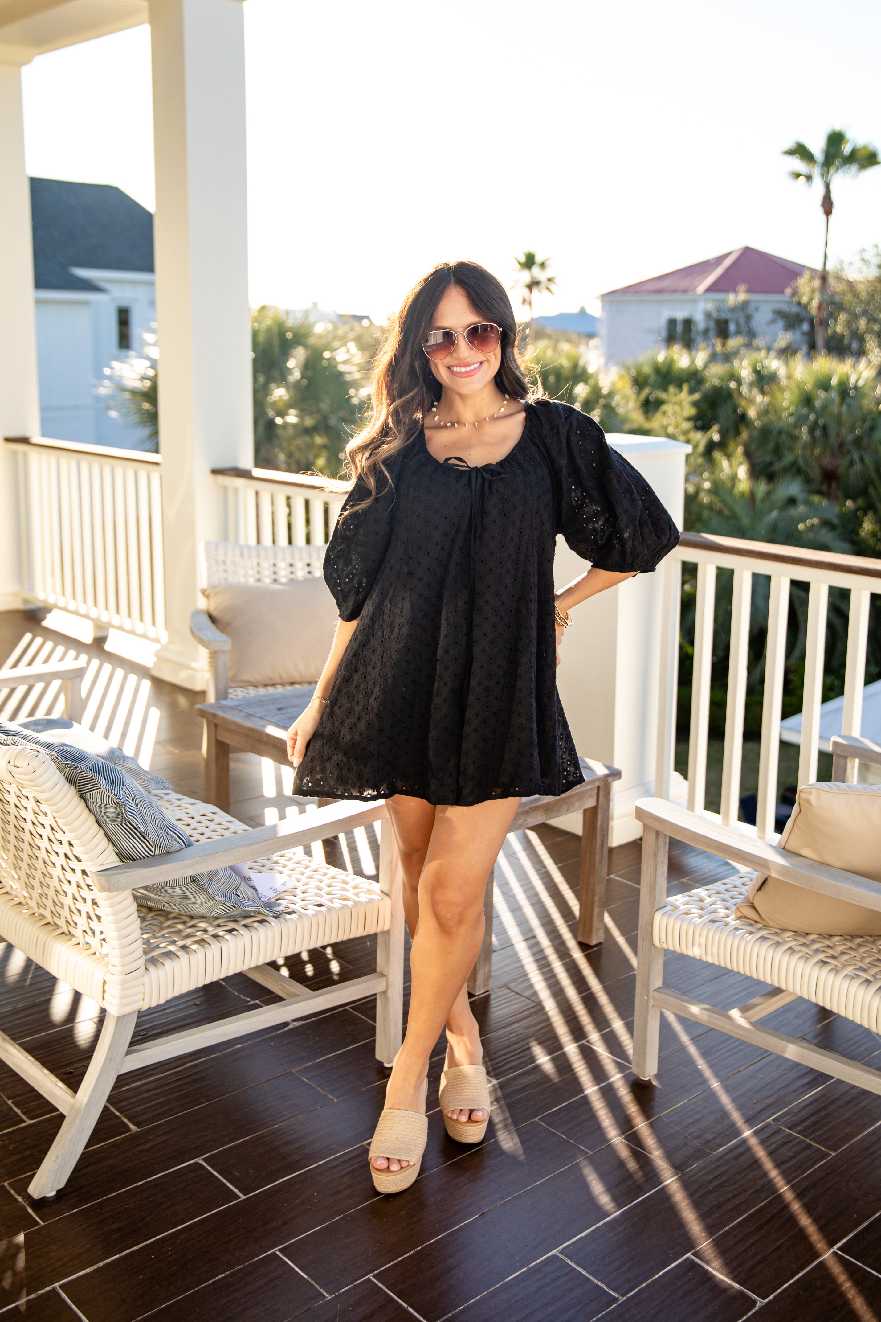 Woman in a black dress standing on a balcony with chairs and a scenic background