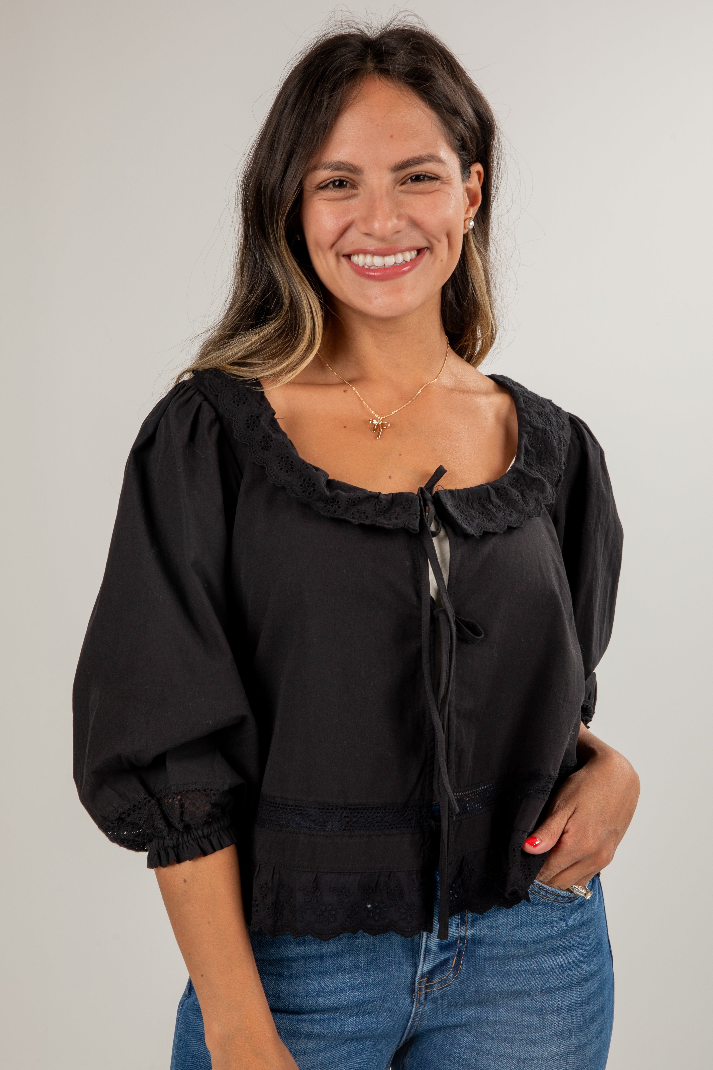 Woman wearing a black blouse with ruffled details and blue jeans on a plain background