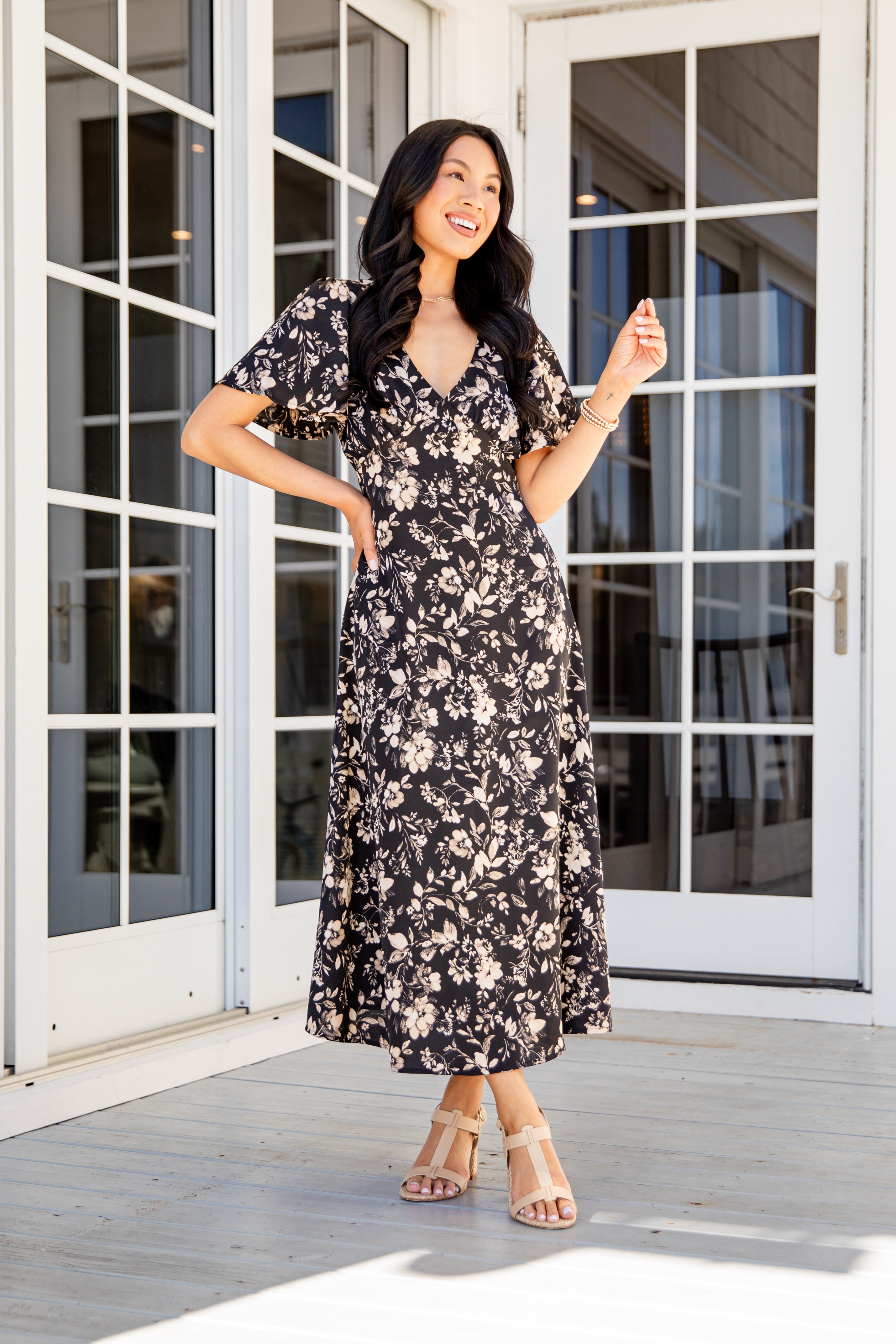 Woman in a floral dress standing on a wooden deck with glass doors in the background