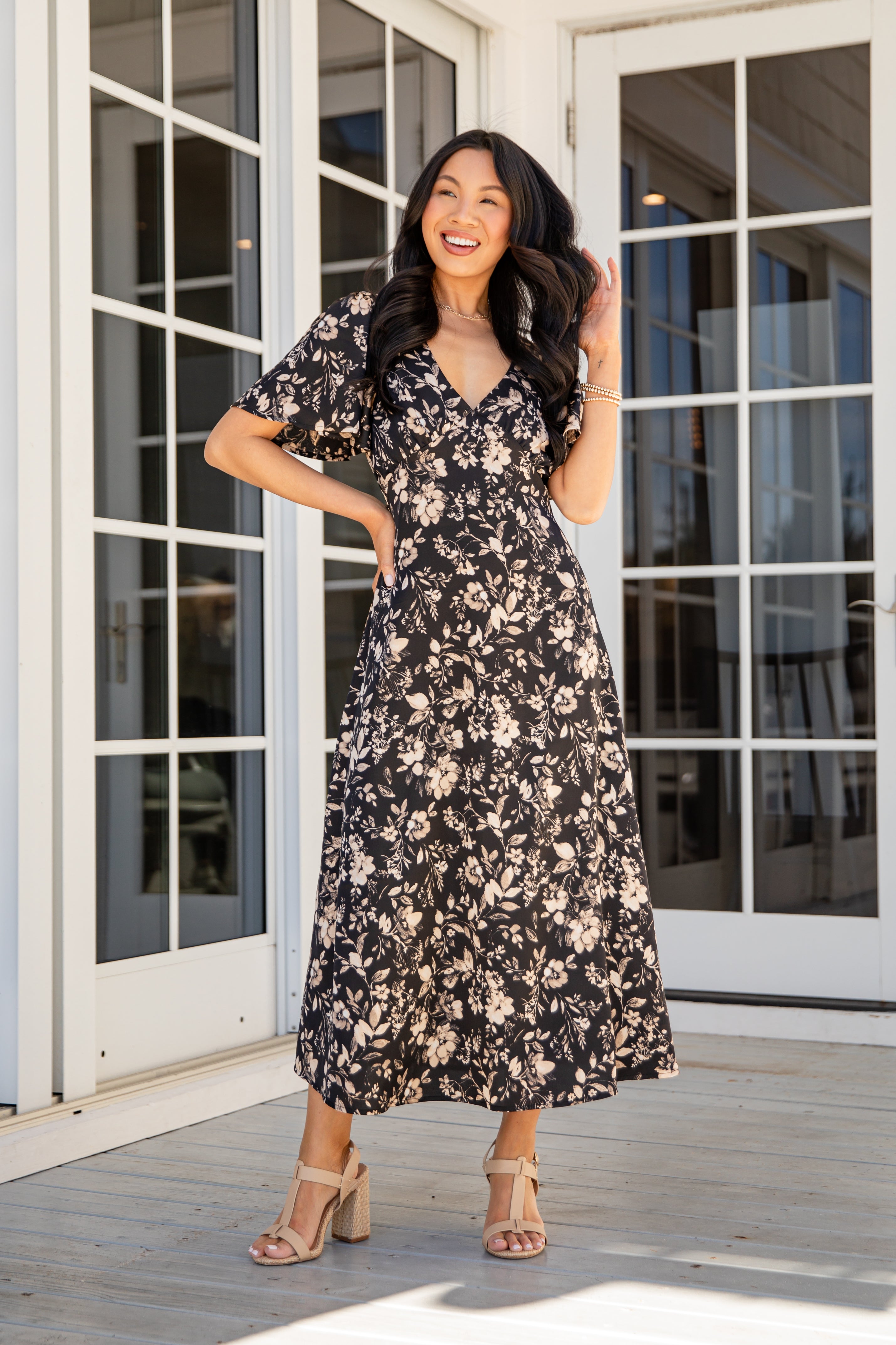 Woman in a floral dress standing on a wooden deck with large glass doors in the background