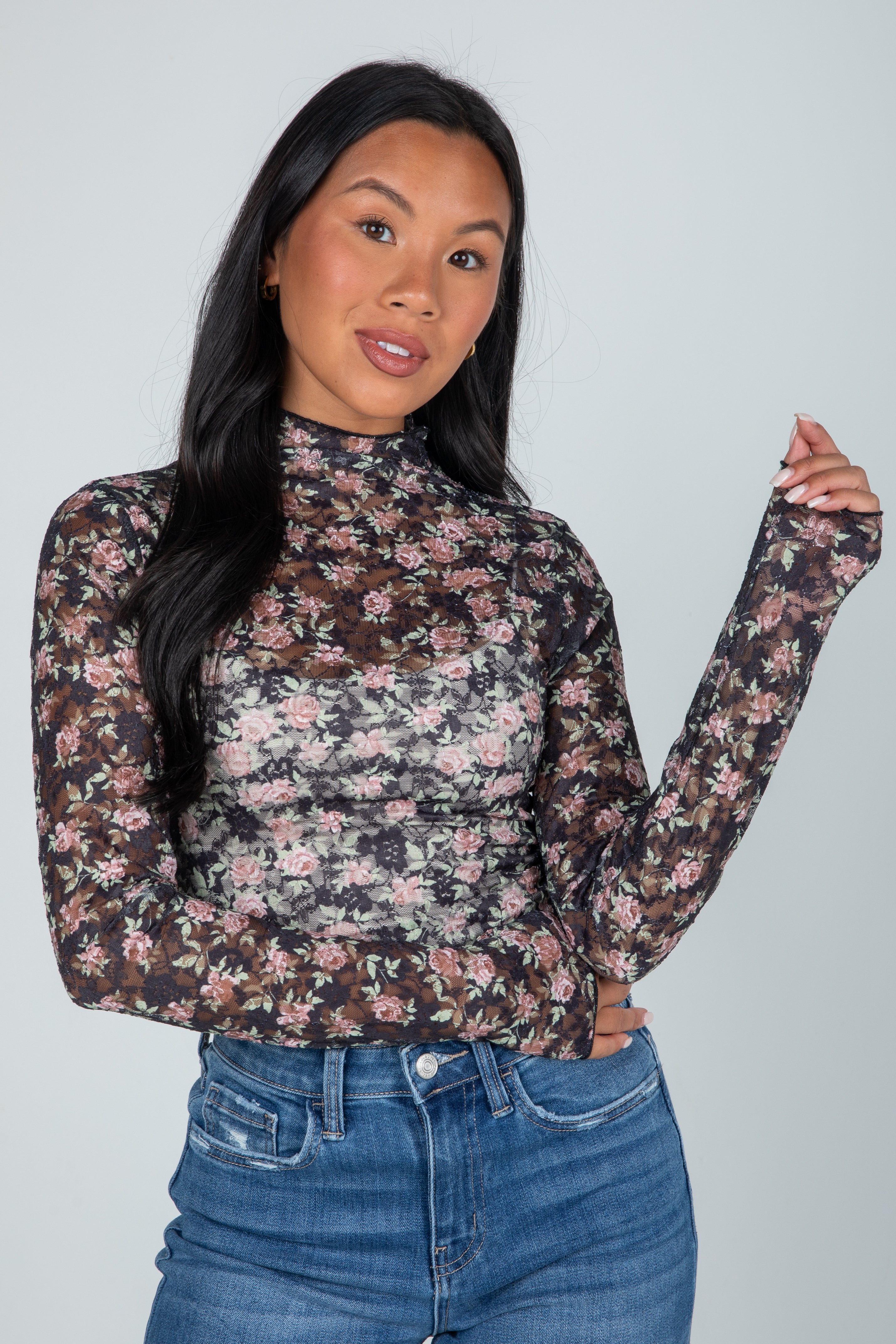 Woman wearing a floral long-sleeve top and jeans against a plain background