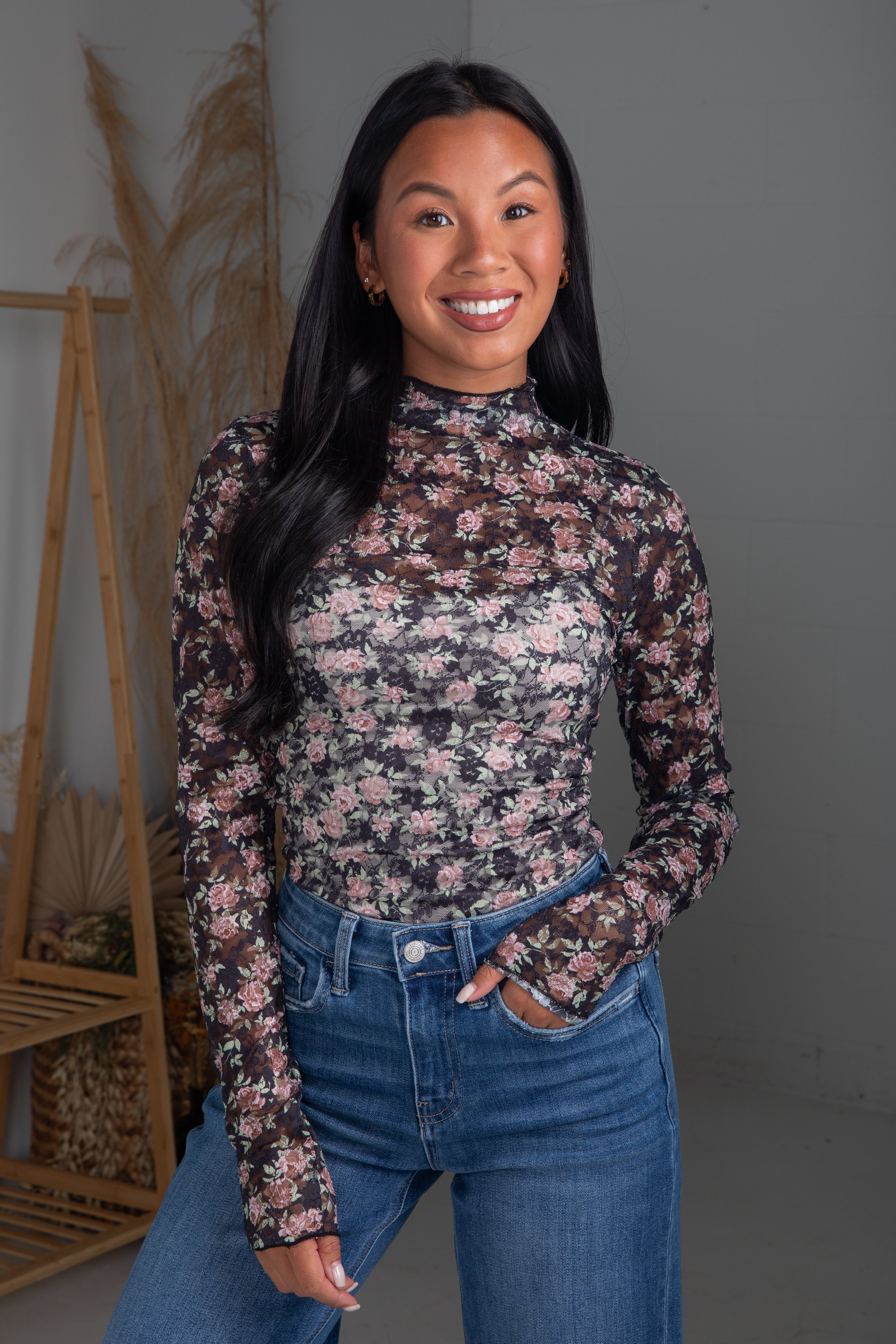 Woman wearing a floral long-sleeve top and blue jeans against a neutral background