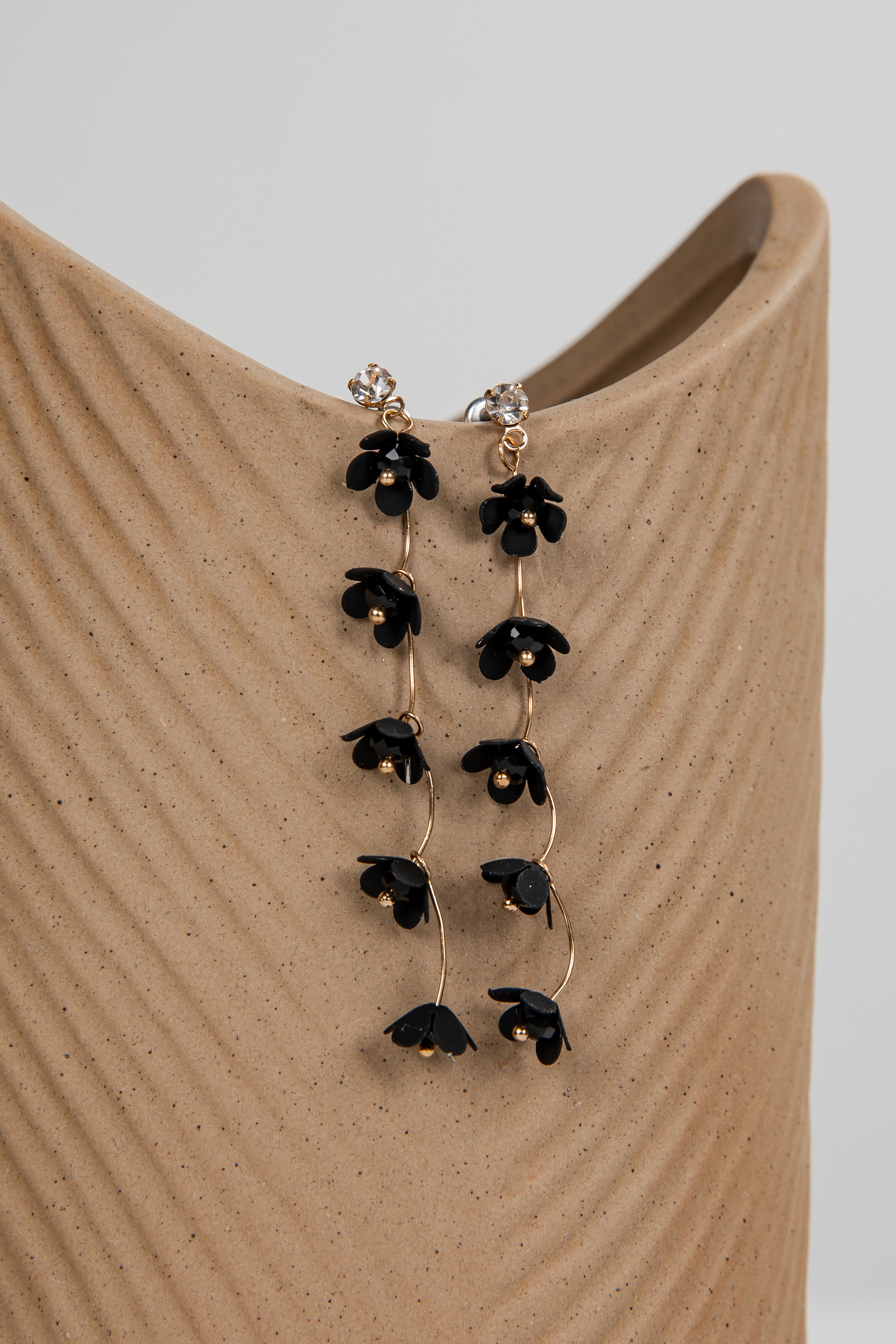 Black floral earrings on a beige stand with a neutral background