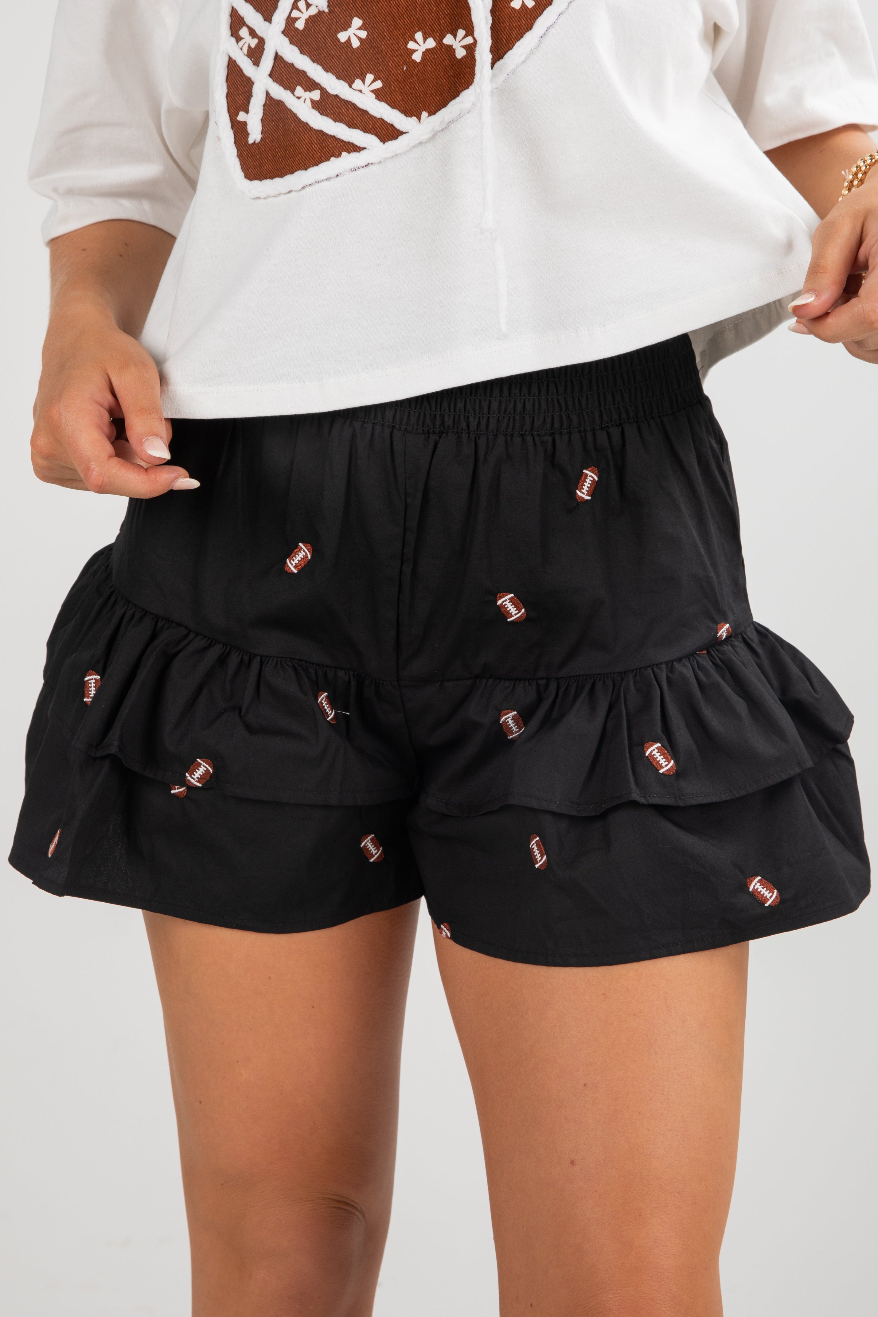 Black ruffled shorts with pink details worn by a person on a plain background
