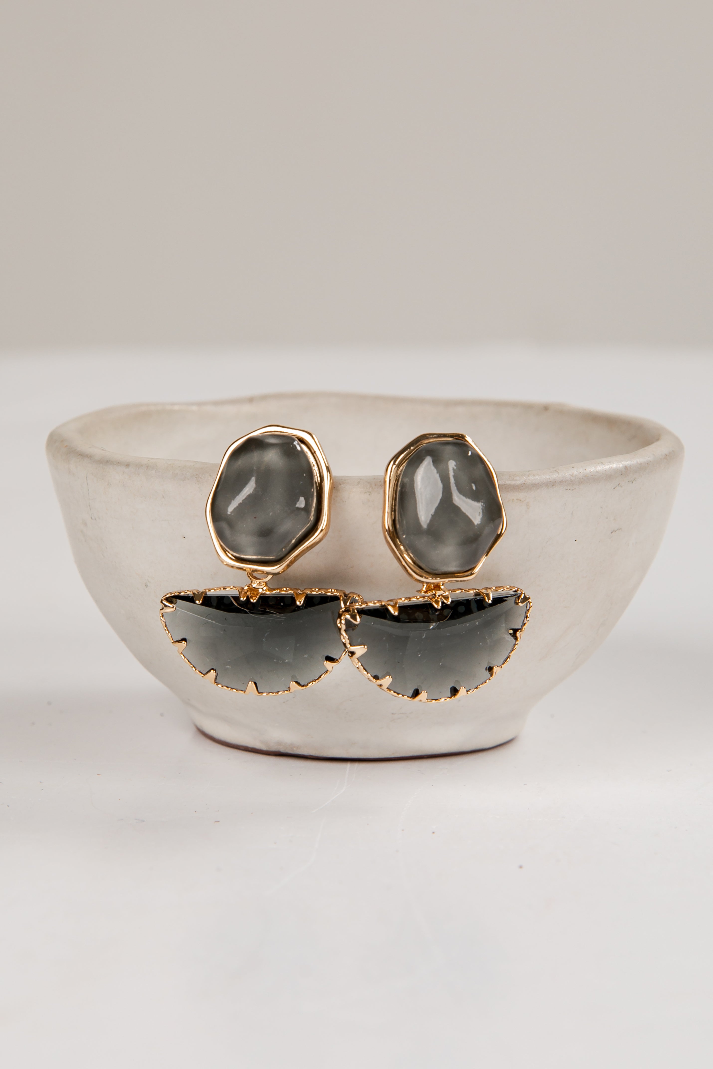 Pair of earrings with gray stones and gold accents on a white surface.