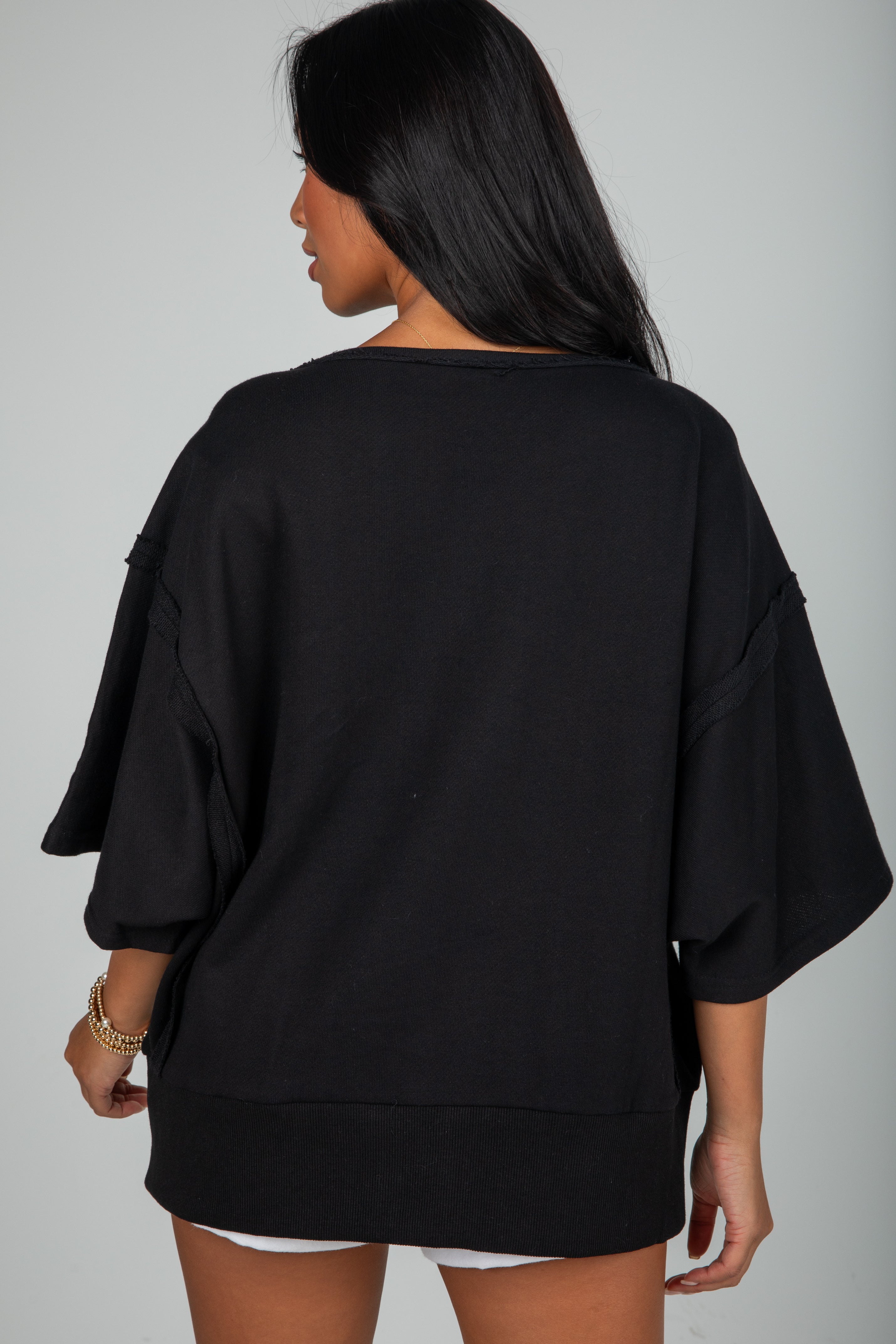 Person wearing a black oversized top and shorts on a gray background