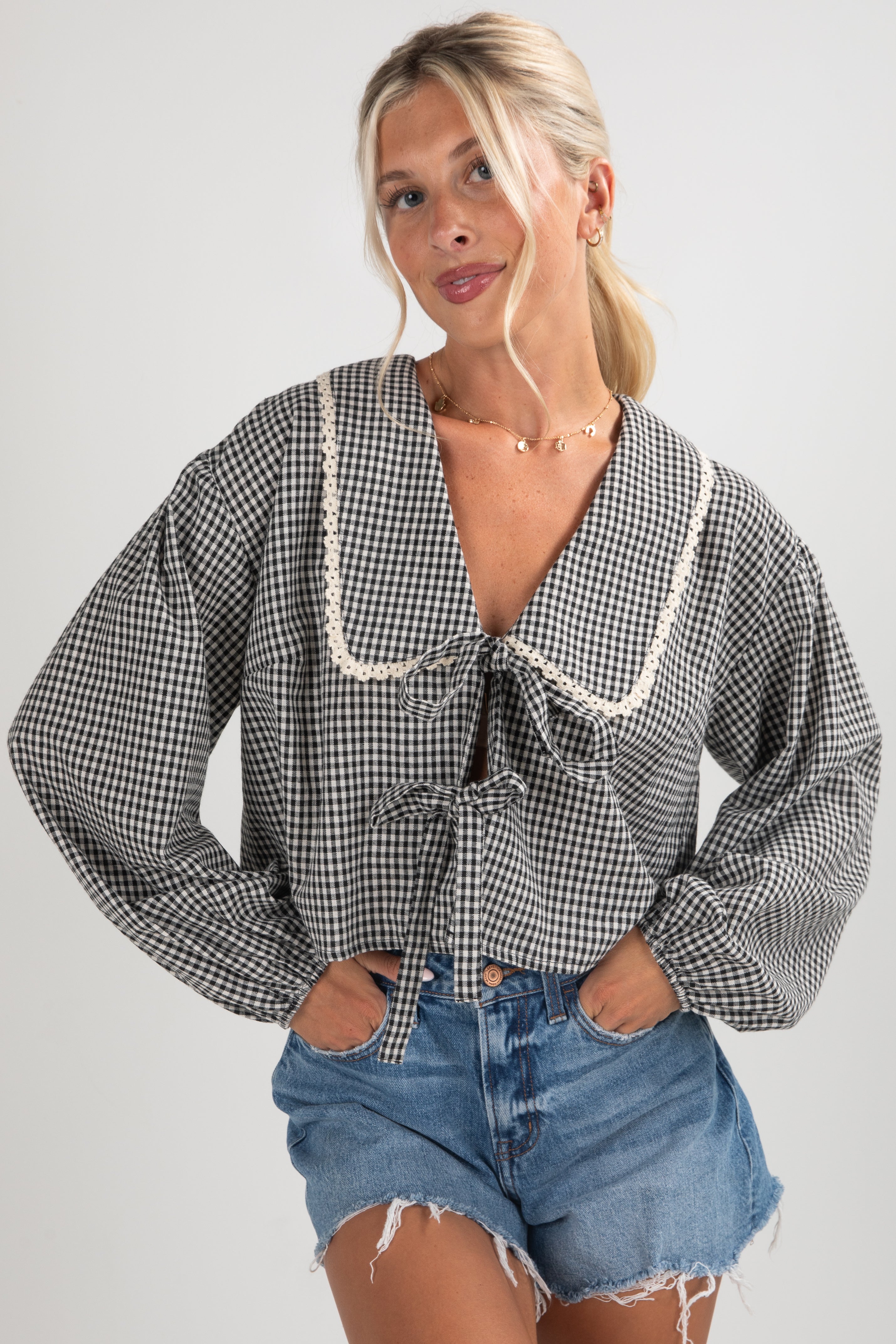 Woman wearing a checkered blouse with lace trim and denim shorts on a plain background