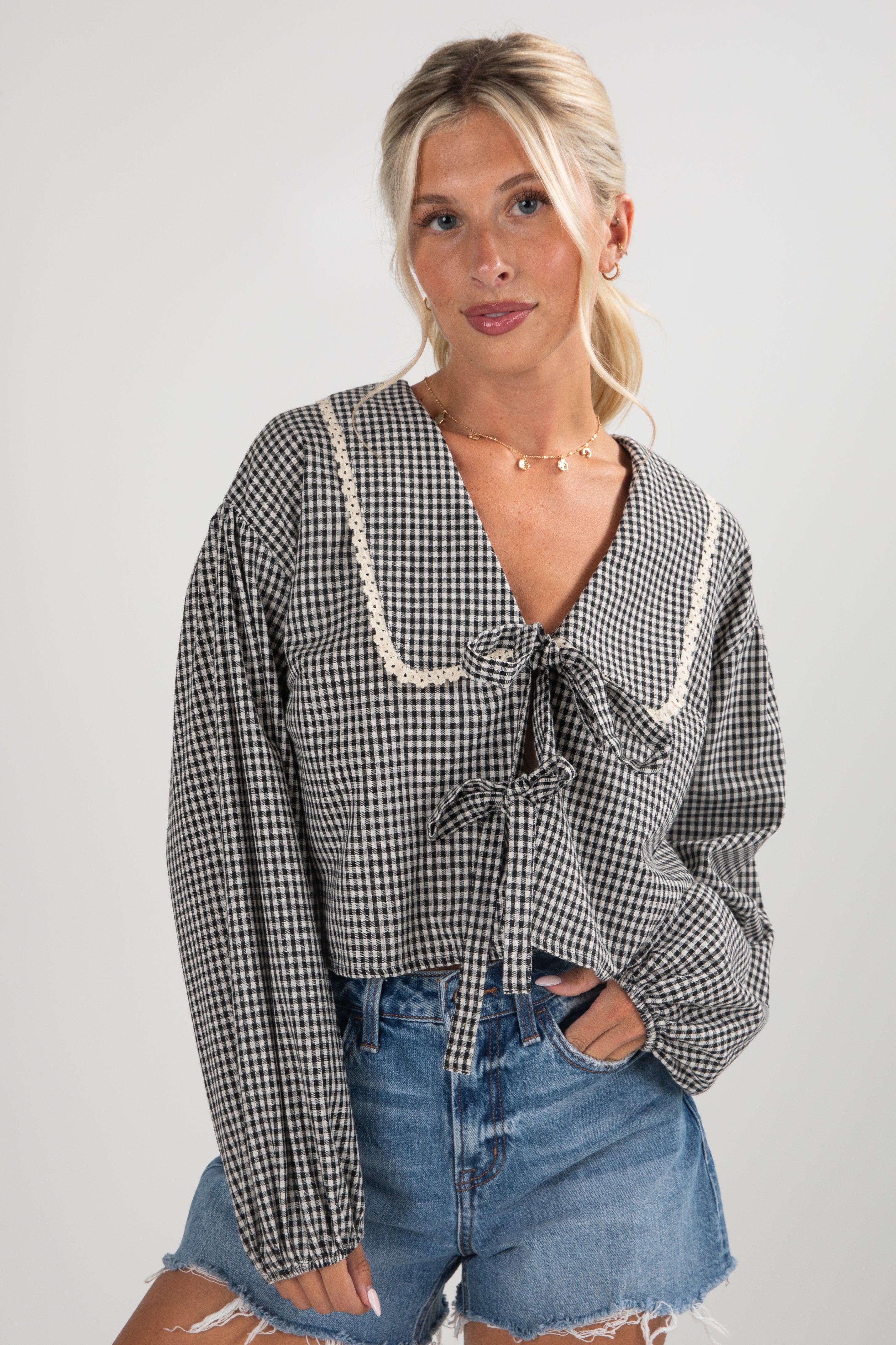 Woman wearing a checkered blouse and denim shorts against a plain background