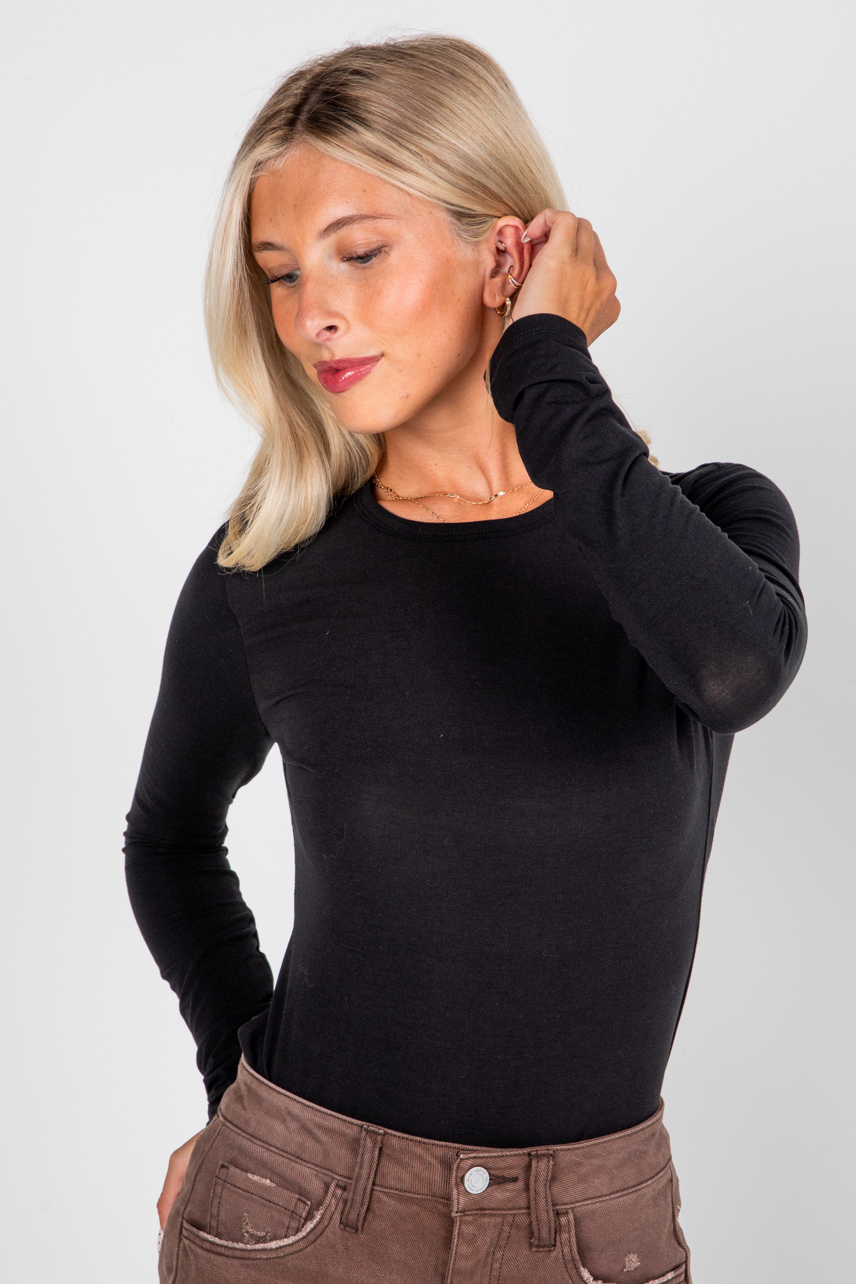 Woman wearing a black long-sleeve top and brown pants against a white background