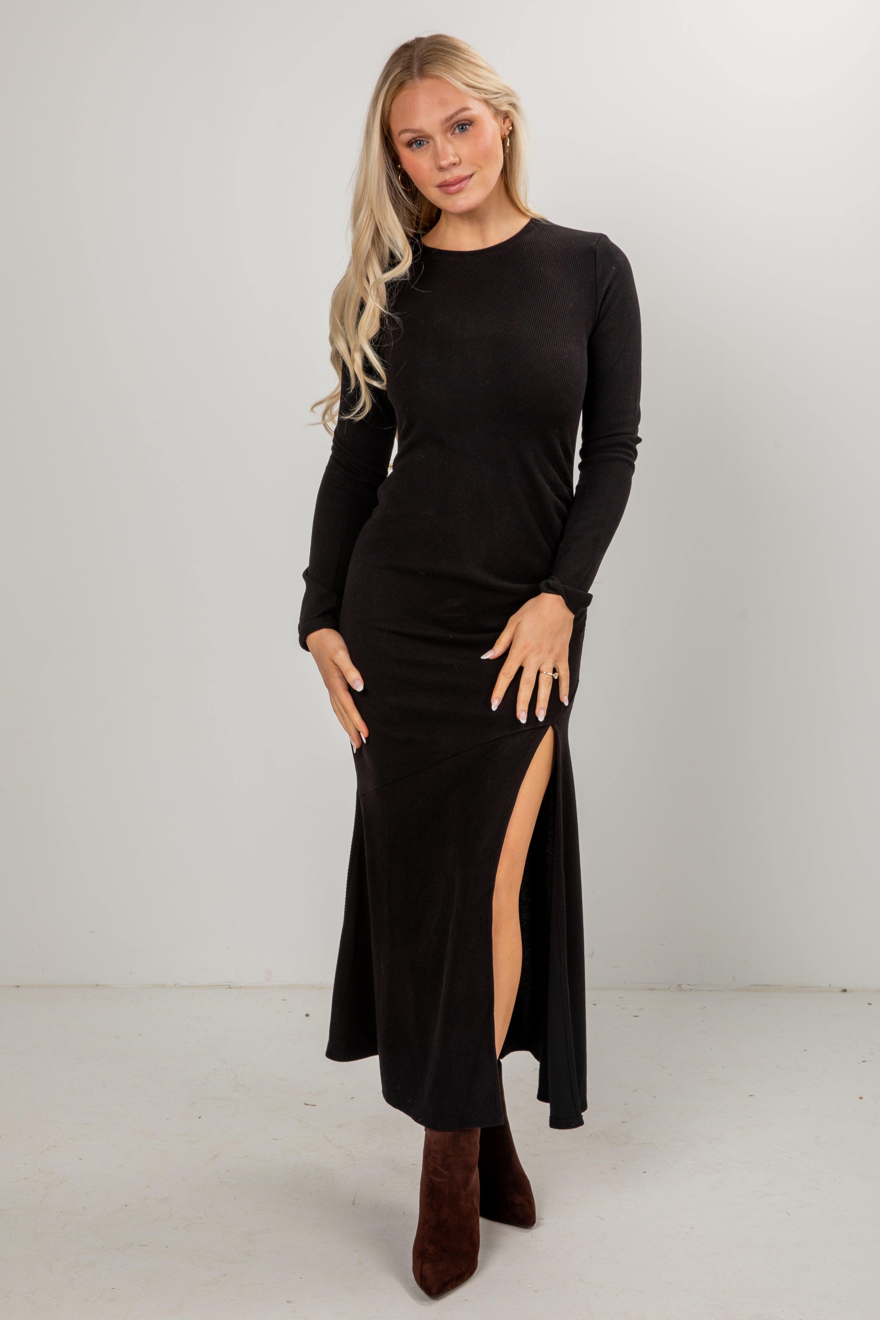Woman wearing a black long-sleeve dress with a slit on a white background