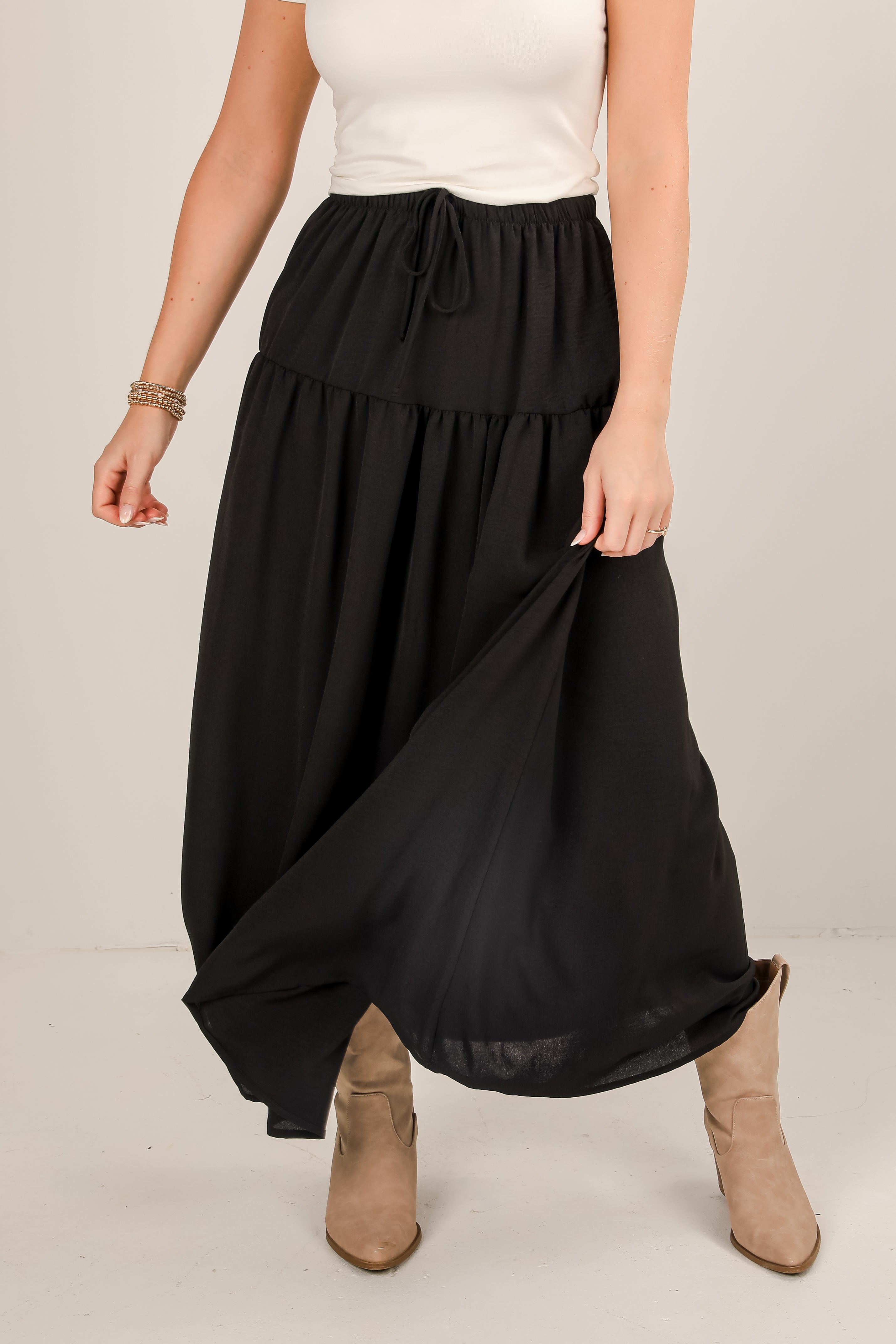 Person wearing a black skirt with a white top and brown boots on a plain background