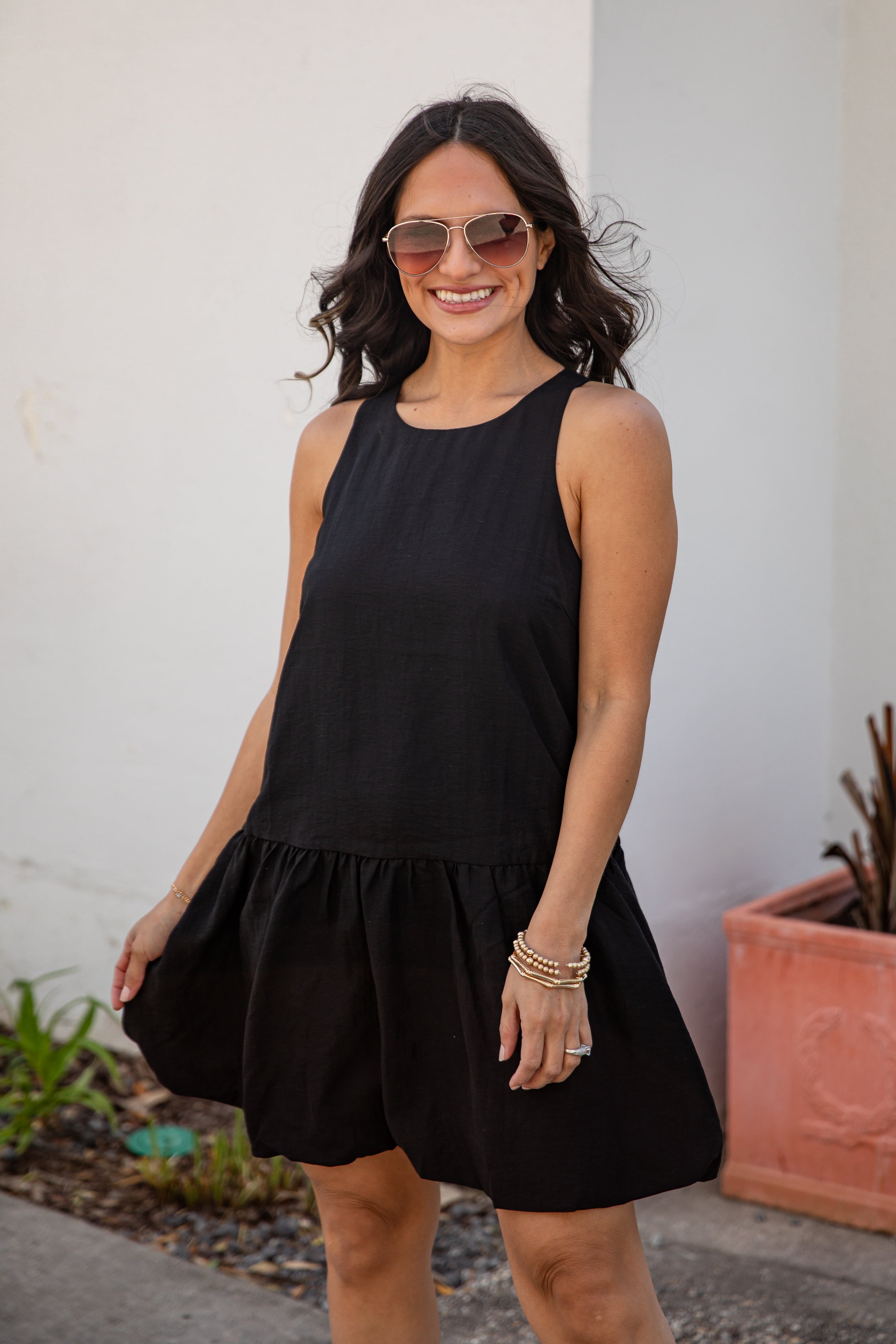Woman wearing a black sleeveless dress standing against a white wall.
