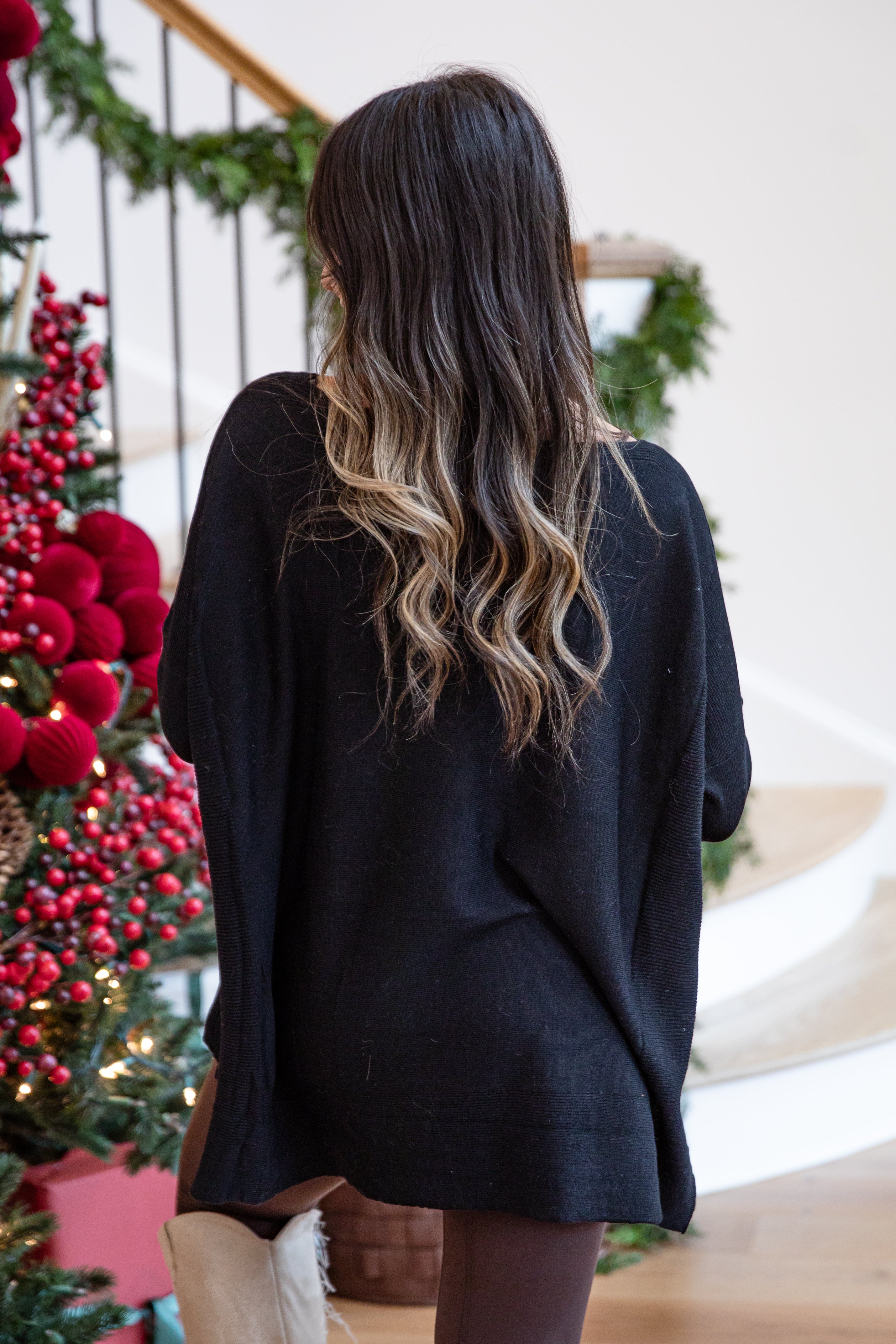 Person wearing a black sweater standing in front of a decorated Christmas tree.