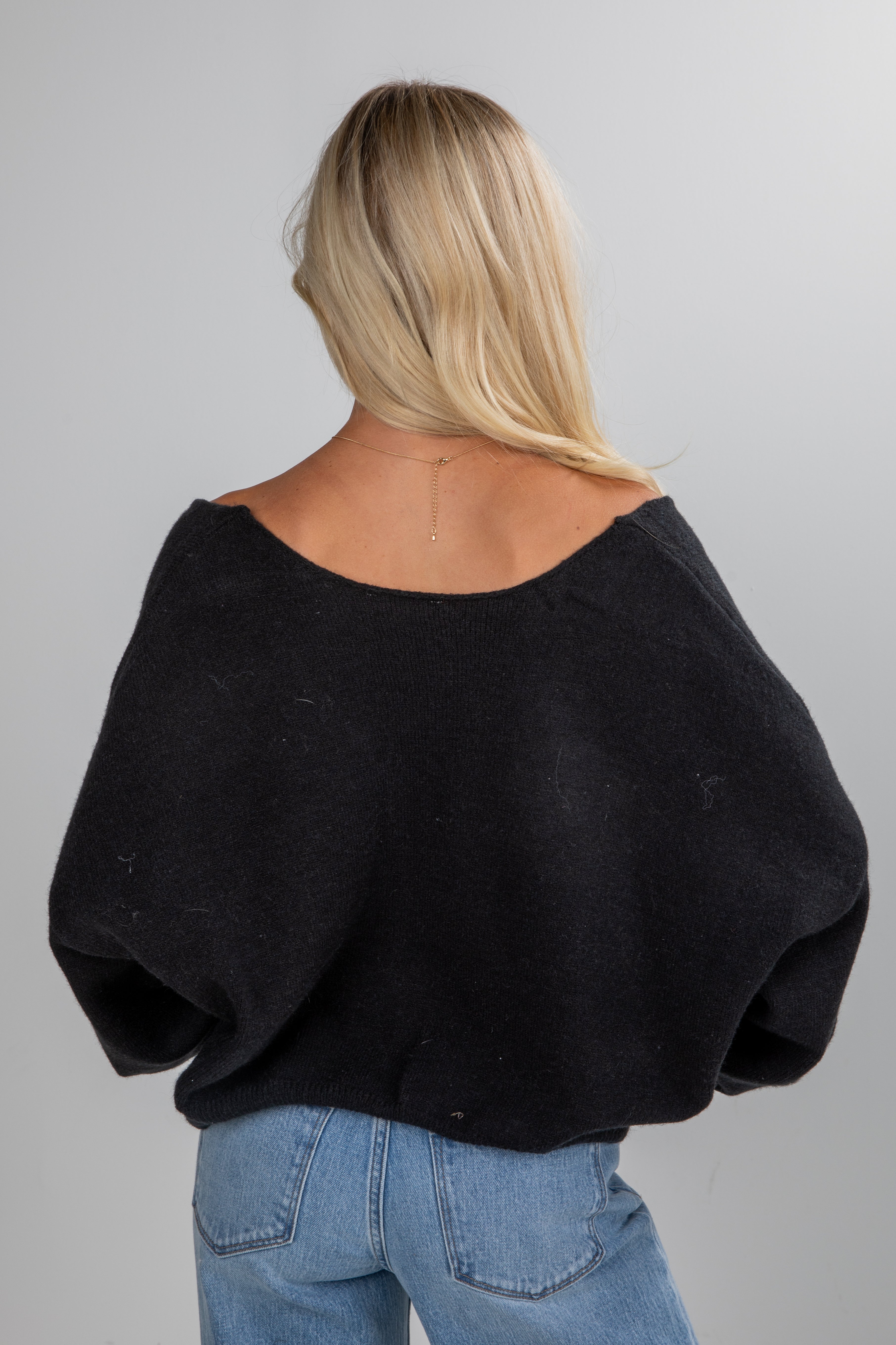 Person wearing a black sweater and blue jeans on a gray background