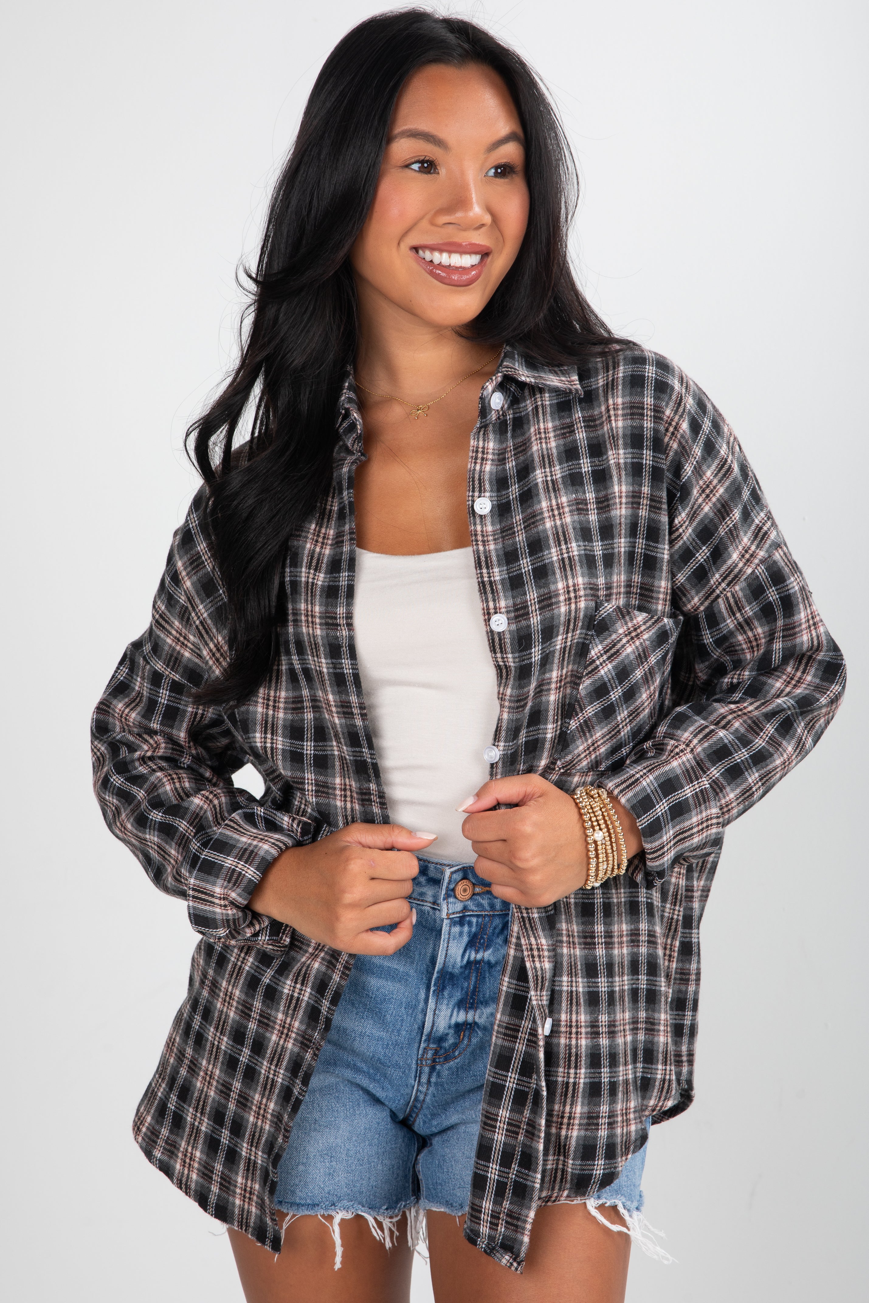 Woman wearing a plaid shirt over a white top and denim shorts on a white background