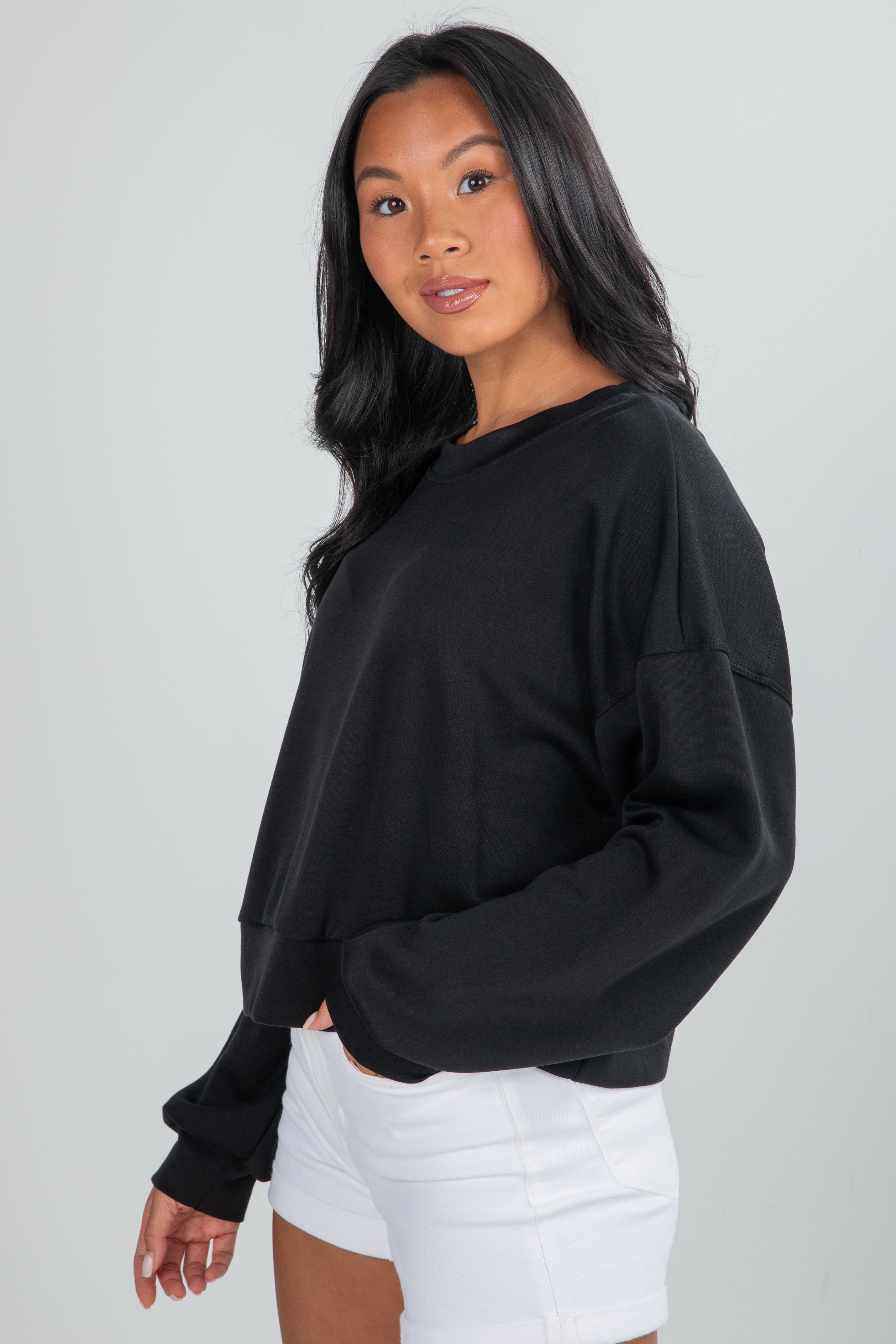 Woman wearing a black oversized sweatshirt and white shorts on a plain background