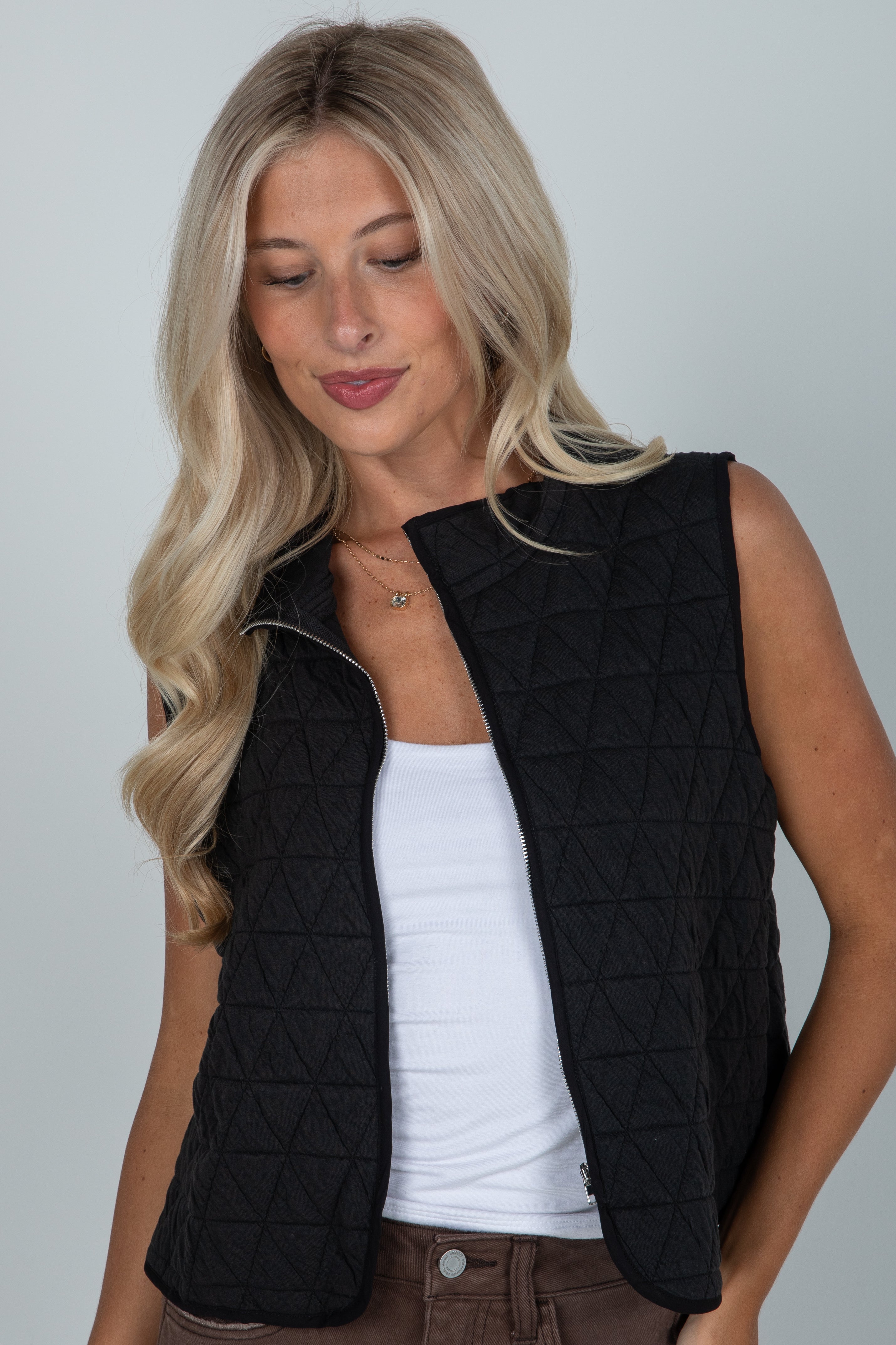 Woman wearing a black quilted vest over a white top on a plain background