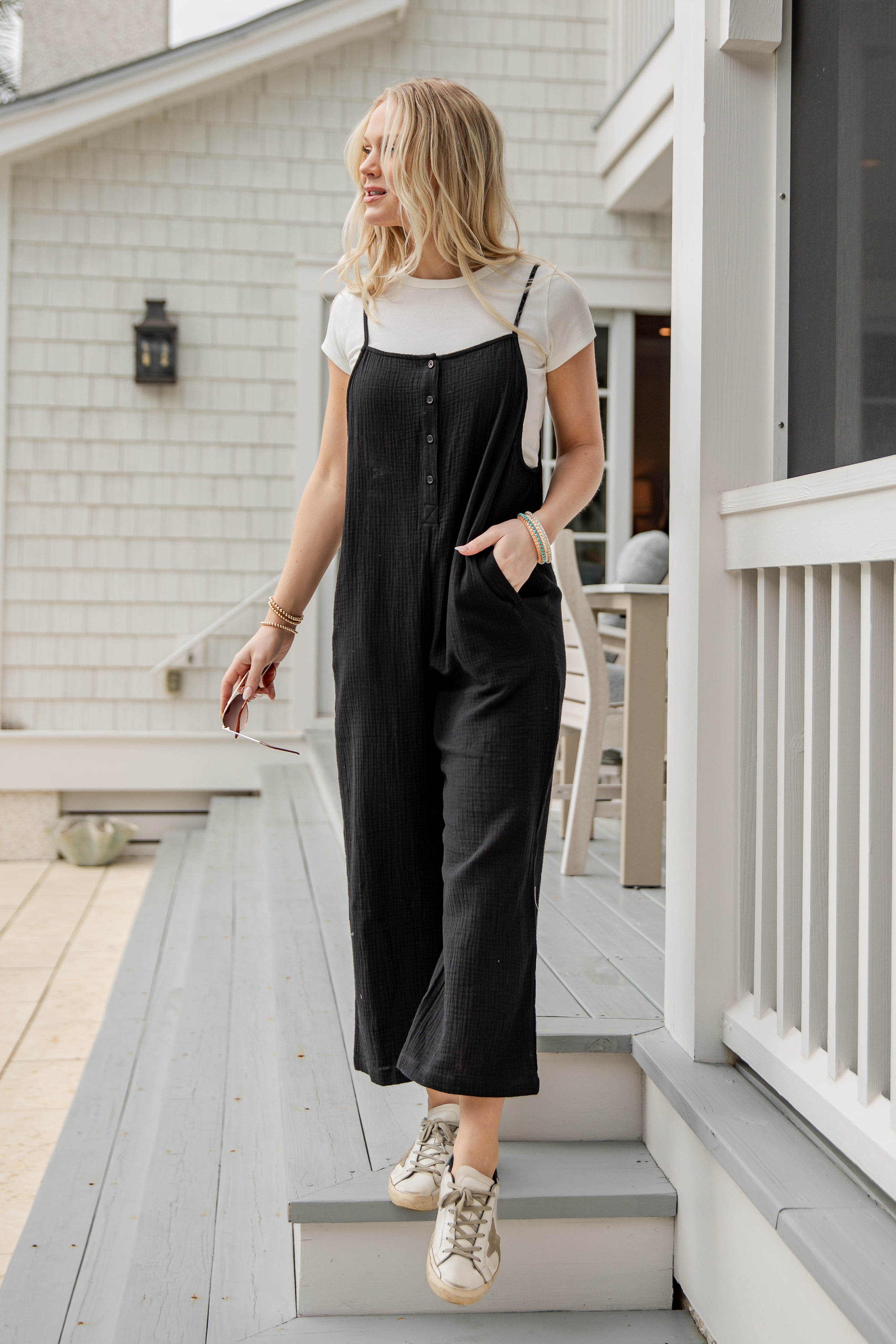 Woman in black overalls and white shirt standing on a porch