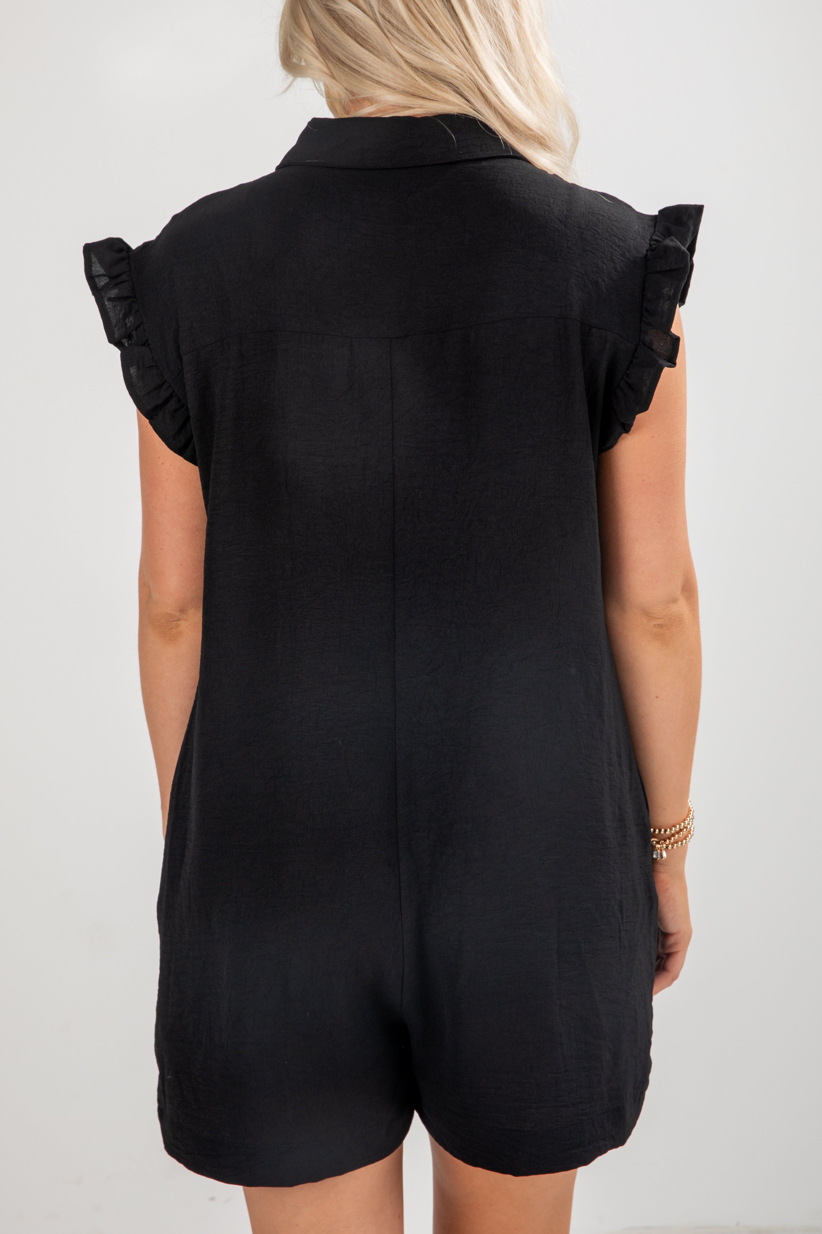 Black romper with ruffled sleeves worn by a person on a white background
