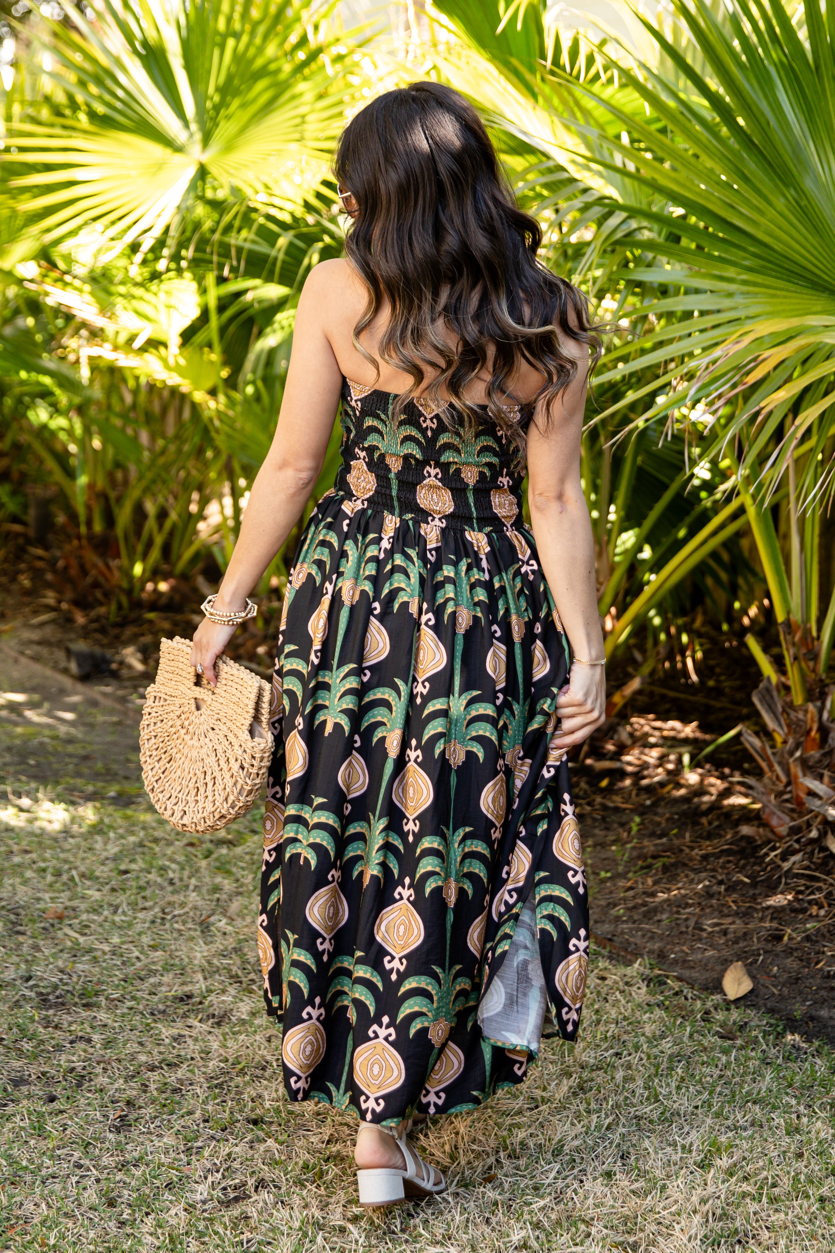 Woman in a tropical patterned dress standing in a garden with palm trees.