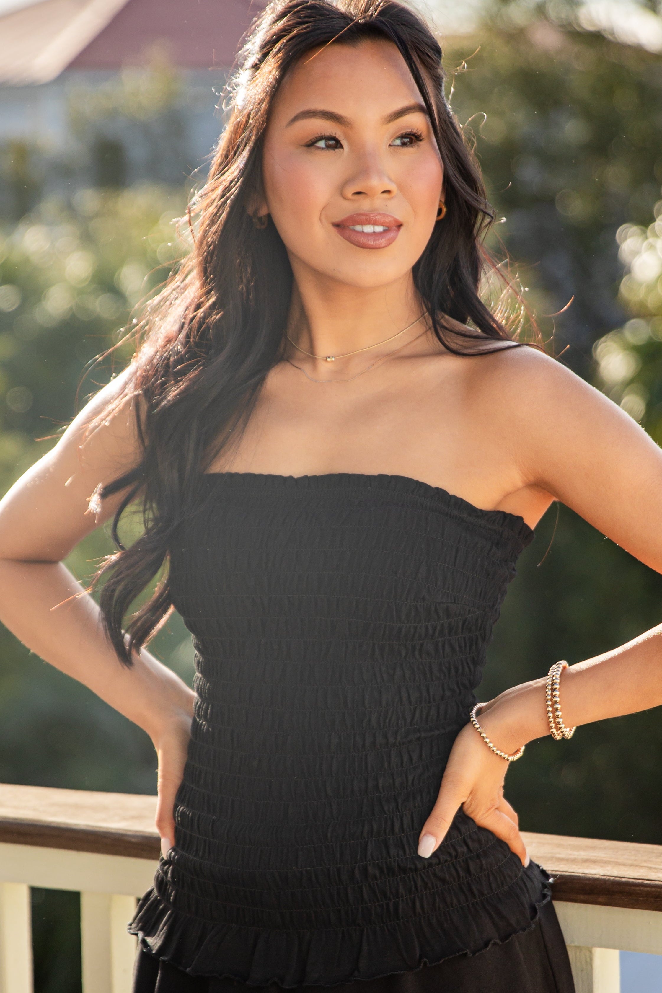 Woman wearing a black strapless dress standing on a balcony with greenery in the background