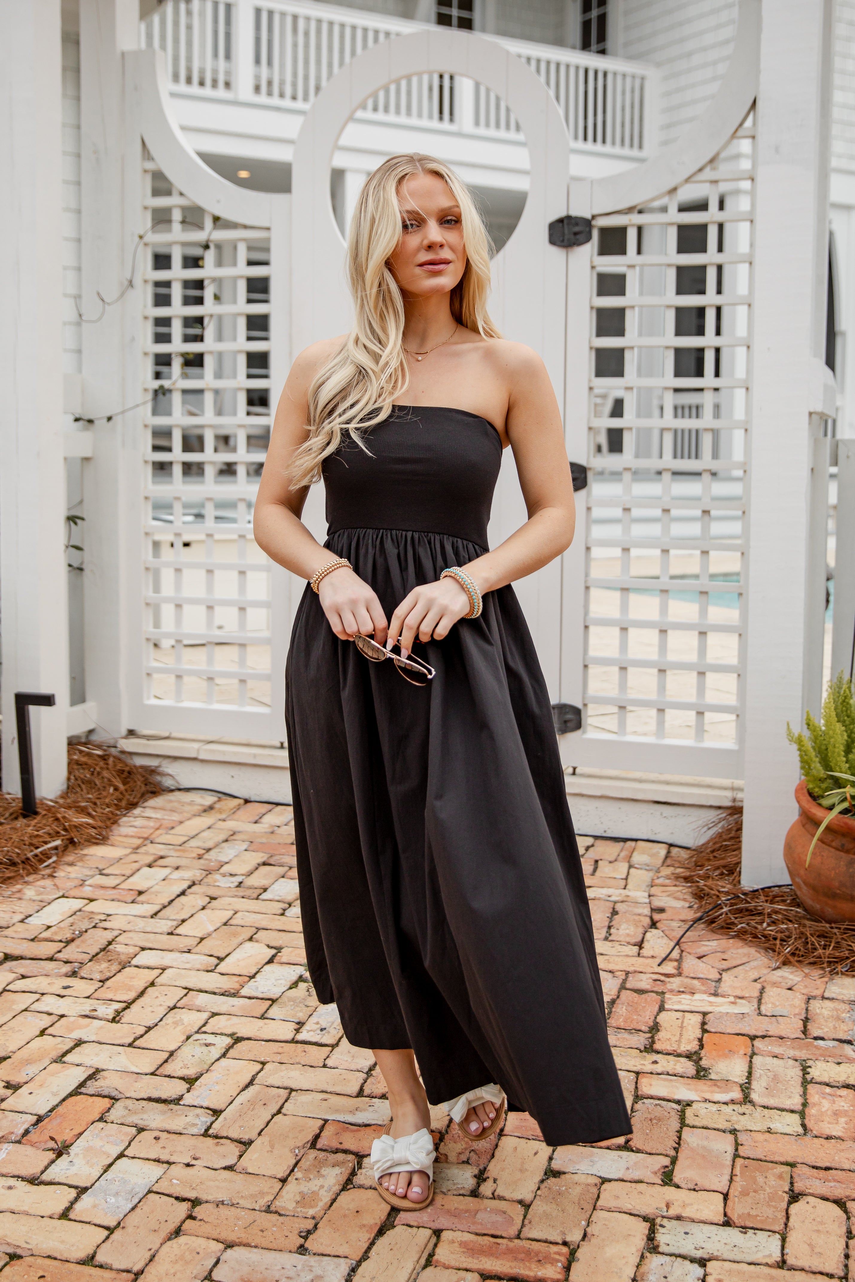 Woman in a black strapless dress standing on a brick patio.