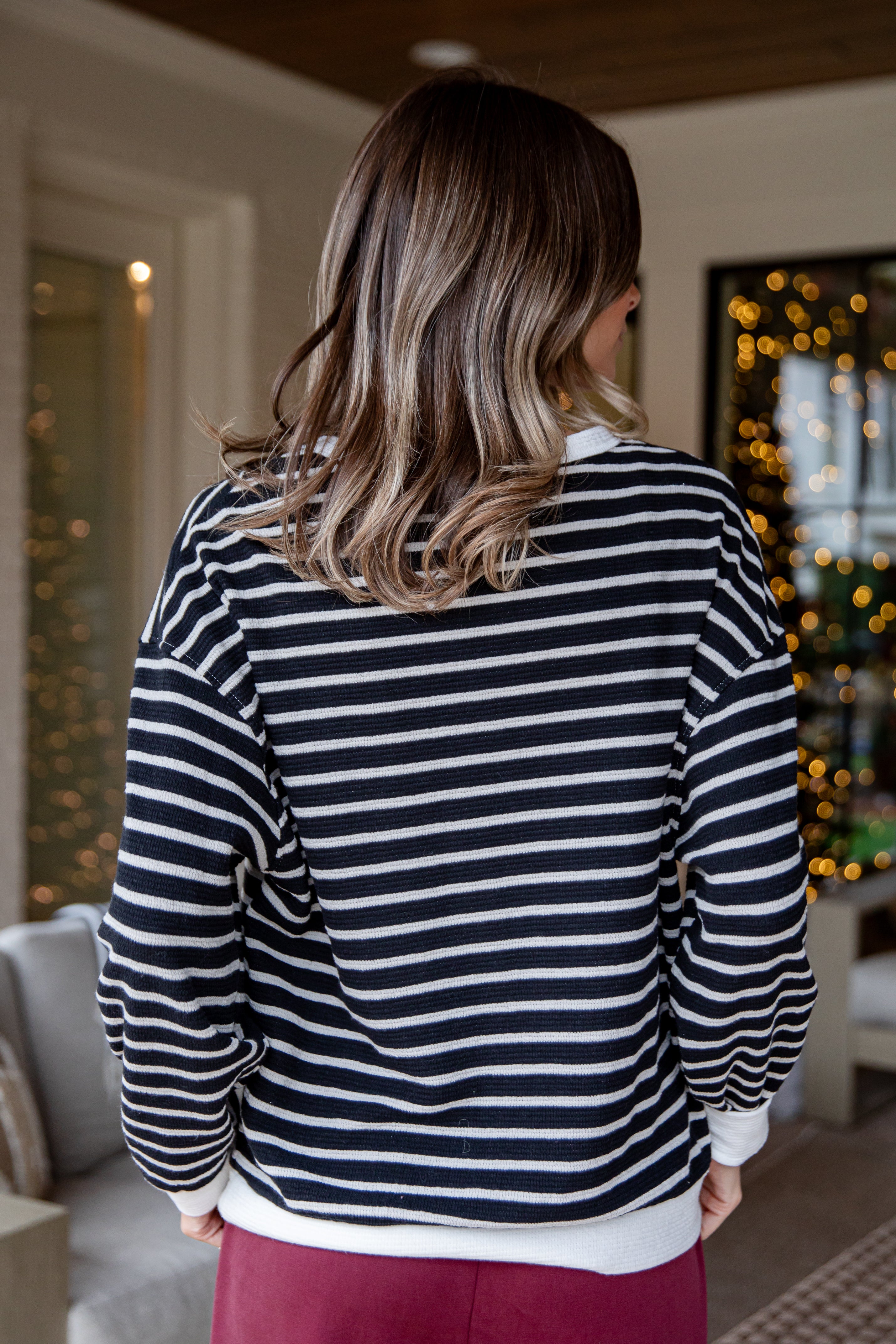 Person wearing a black and white striped sweater in a room with festive decorations.