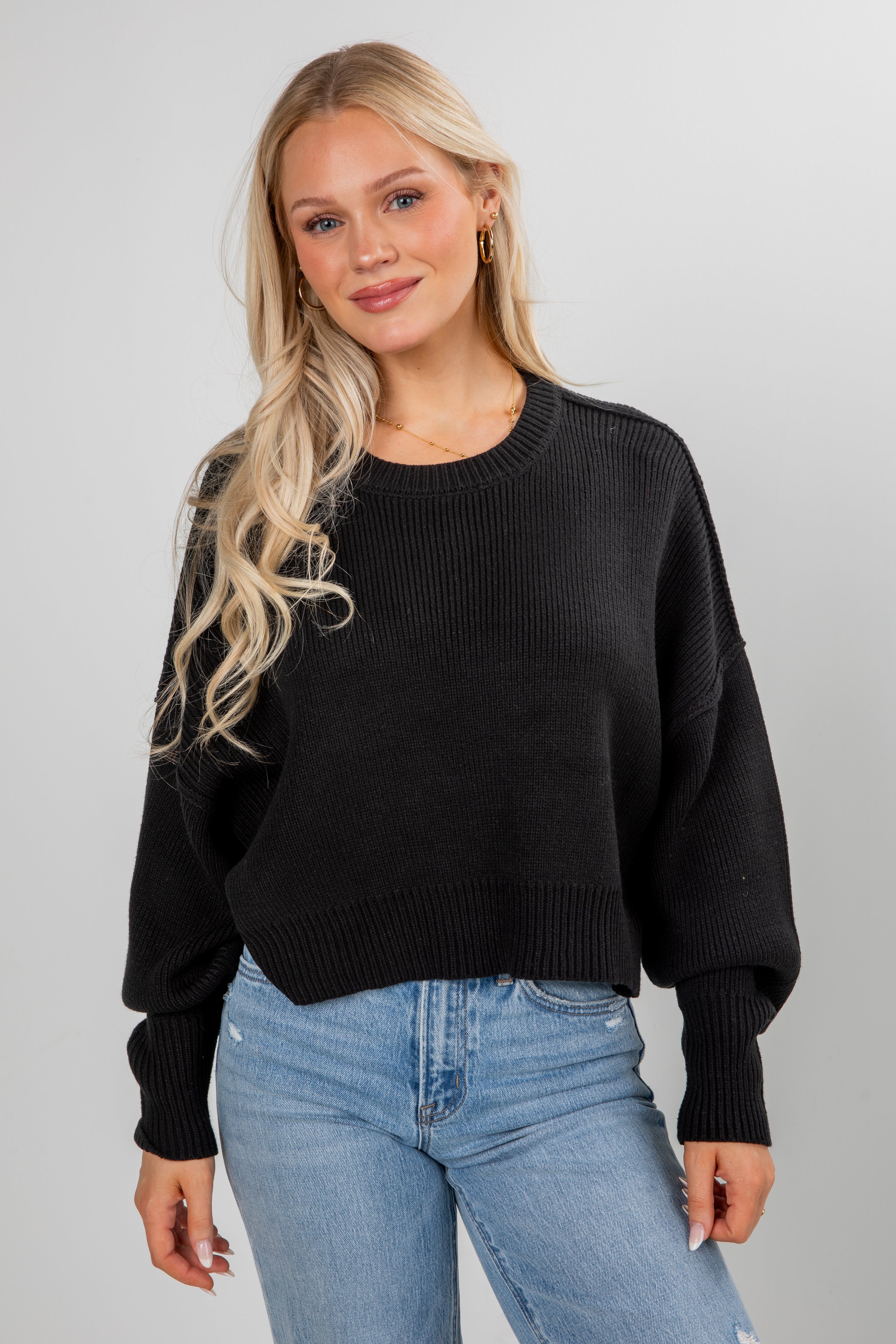 Woman wearing a black sweater and blue jeans against a gray background