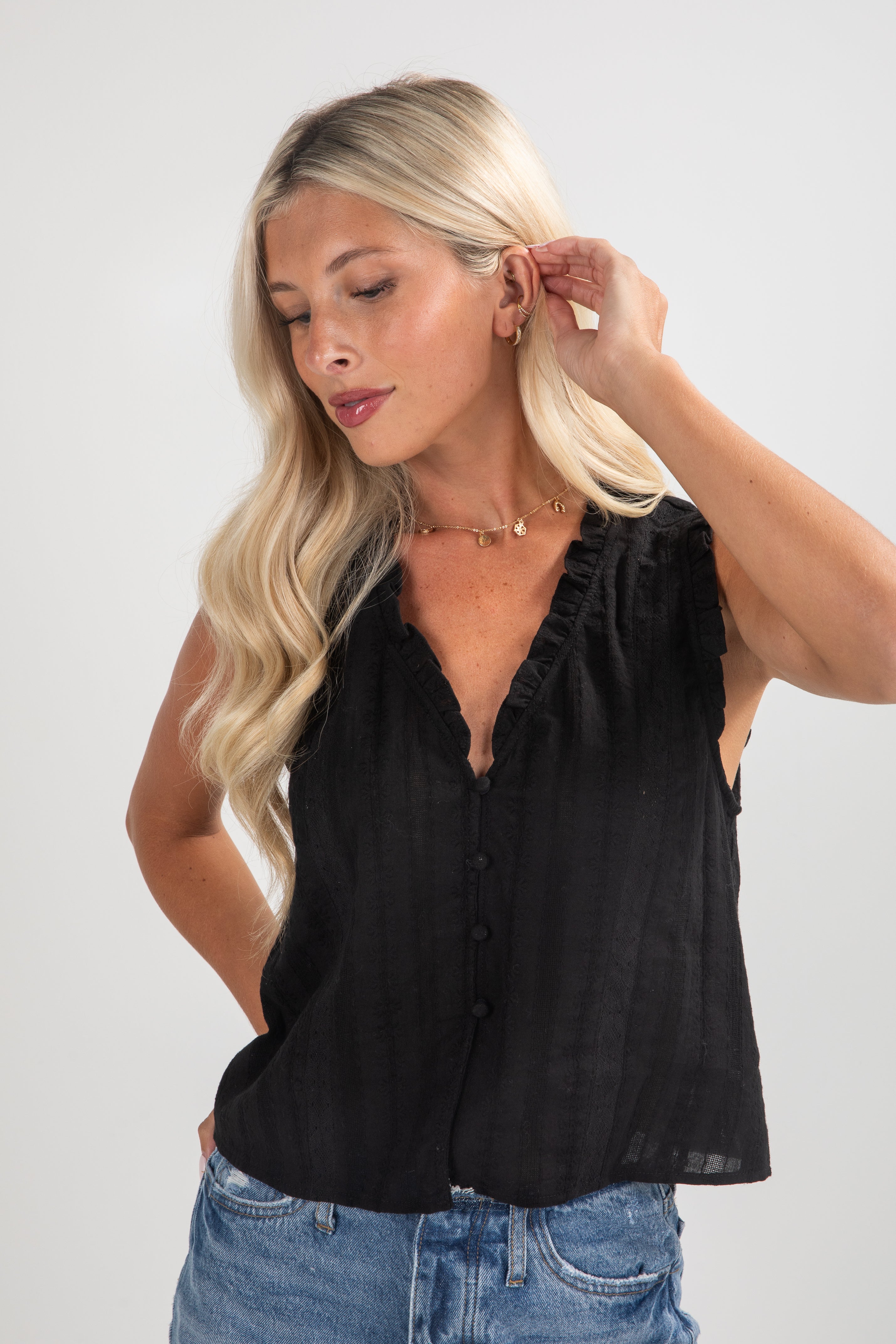 Woman wearing a black sleeveless top and blue jeans on a white background