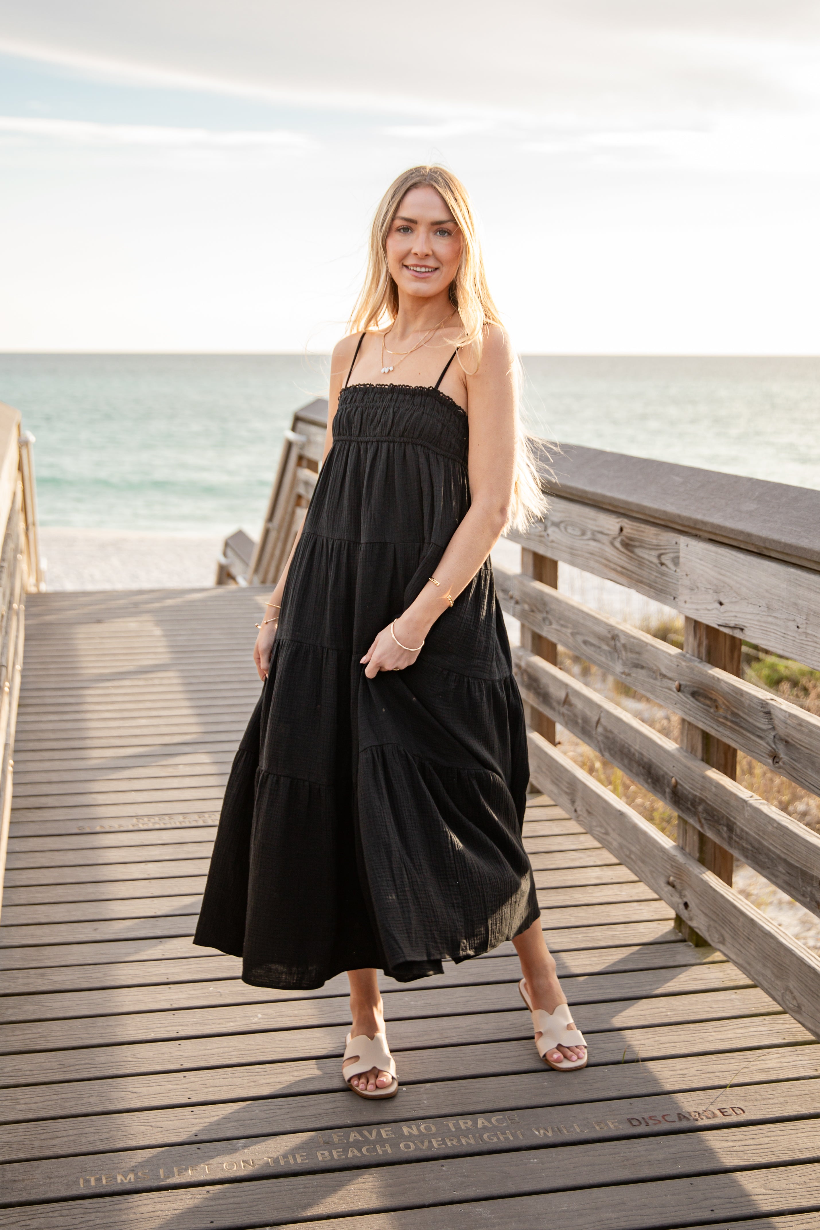 Woman in a black dress standing on a wooden pier by the ocean.