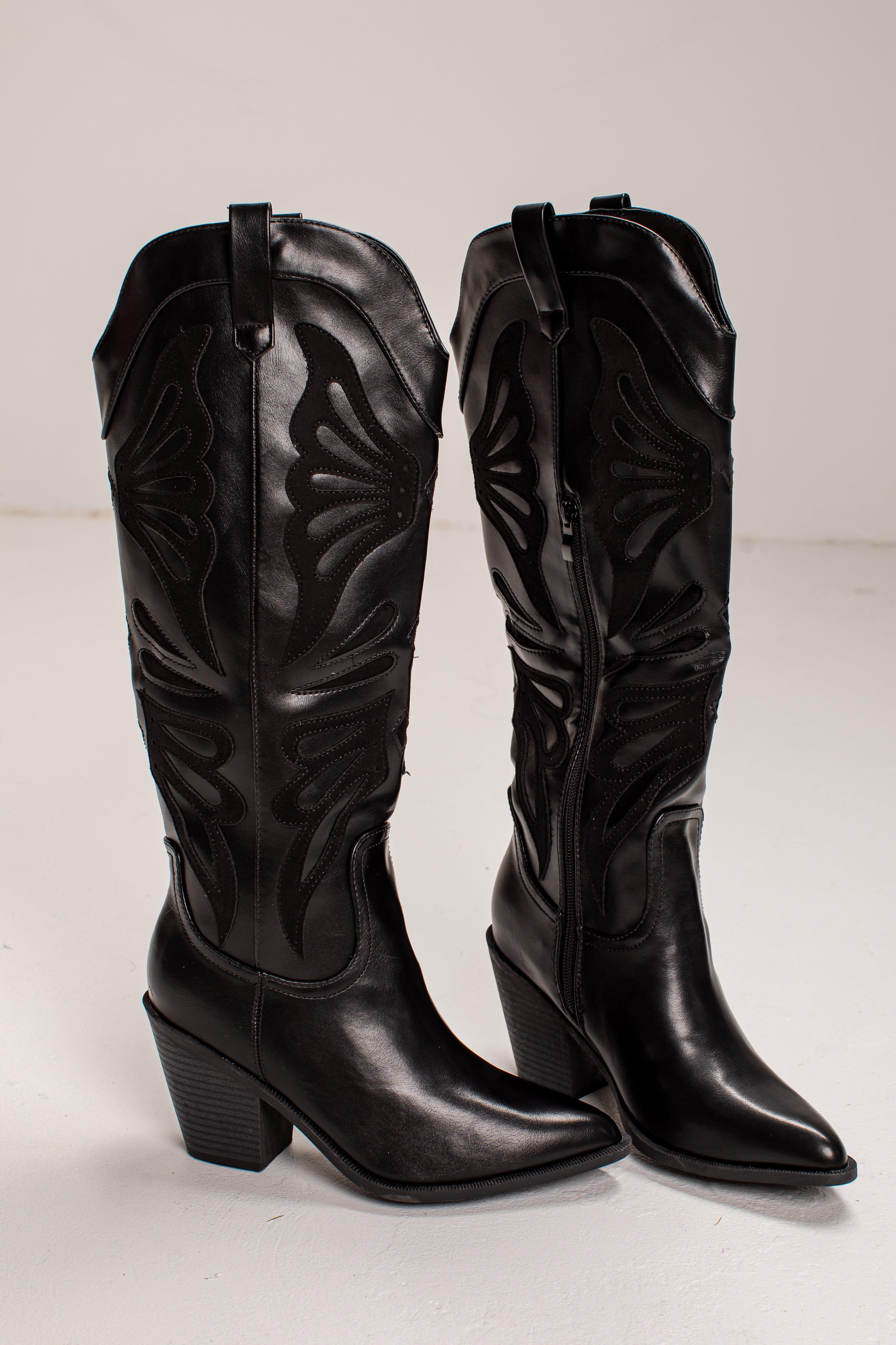A pair of black leather knee-high cowboy boots with pointed toes, low block heels, and decorative western-style stitching, shown against a plain light background.