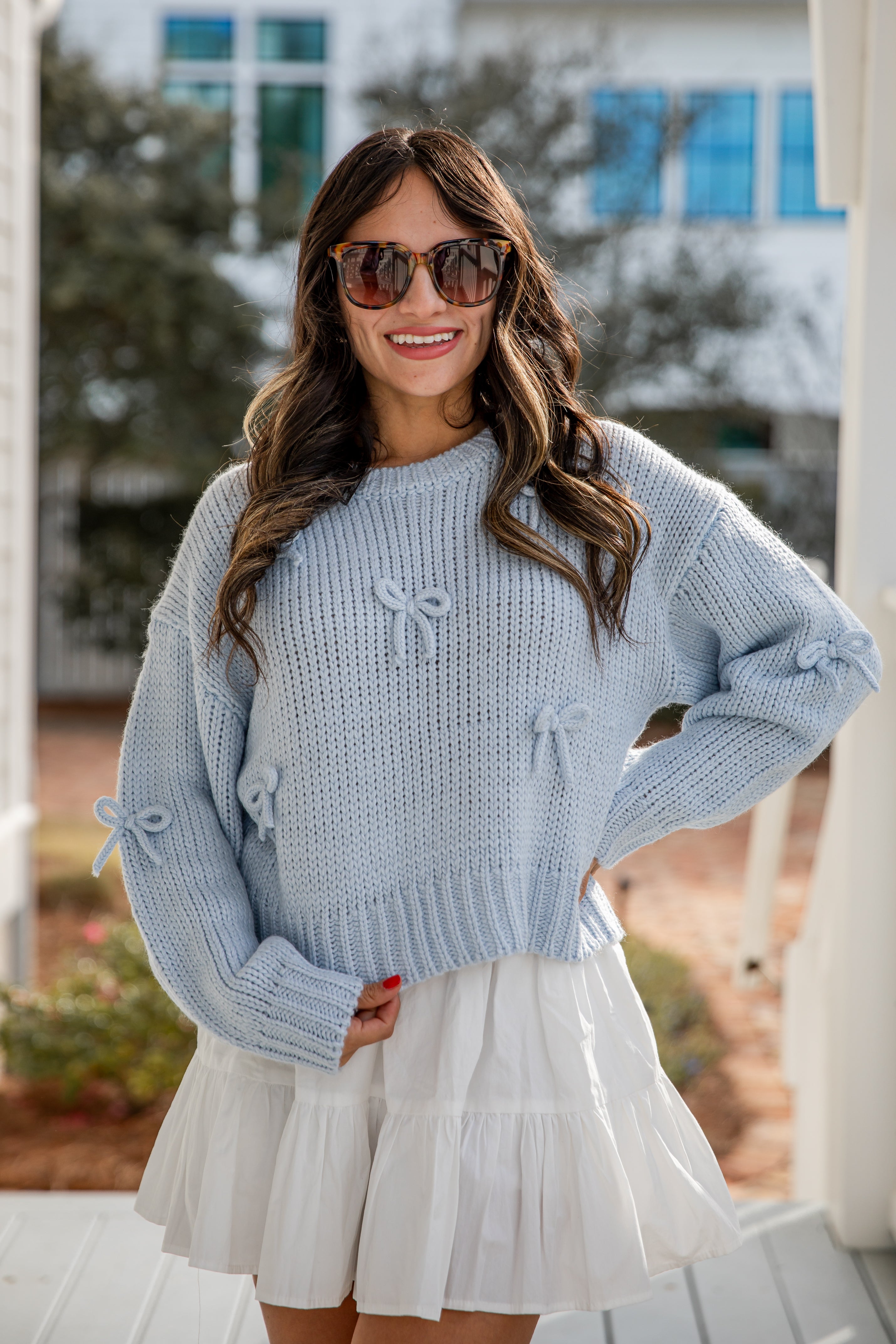 Woman wearing a light blue sweater and white skirt outdoors