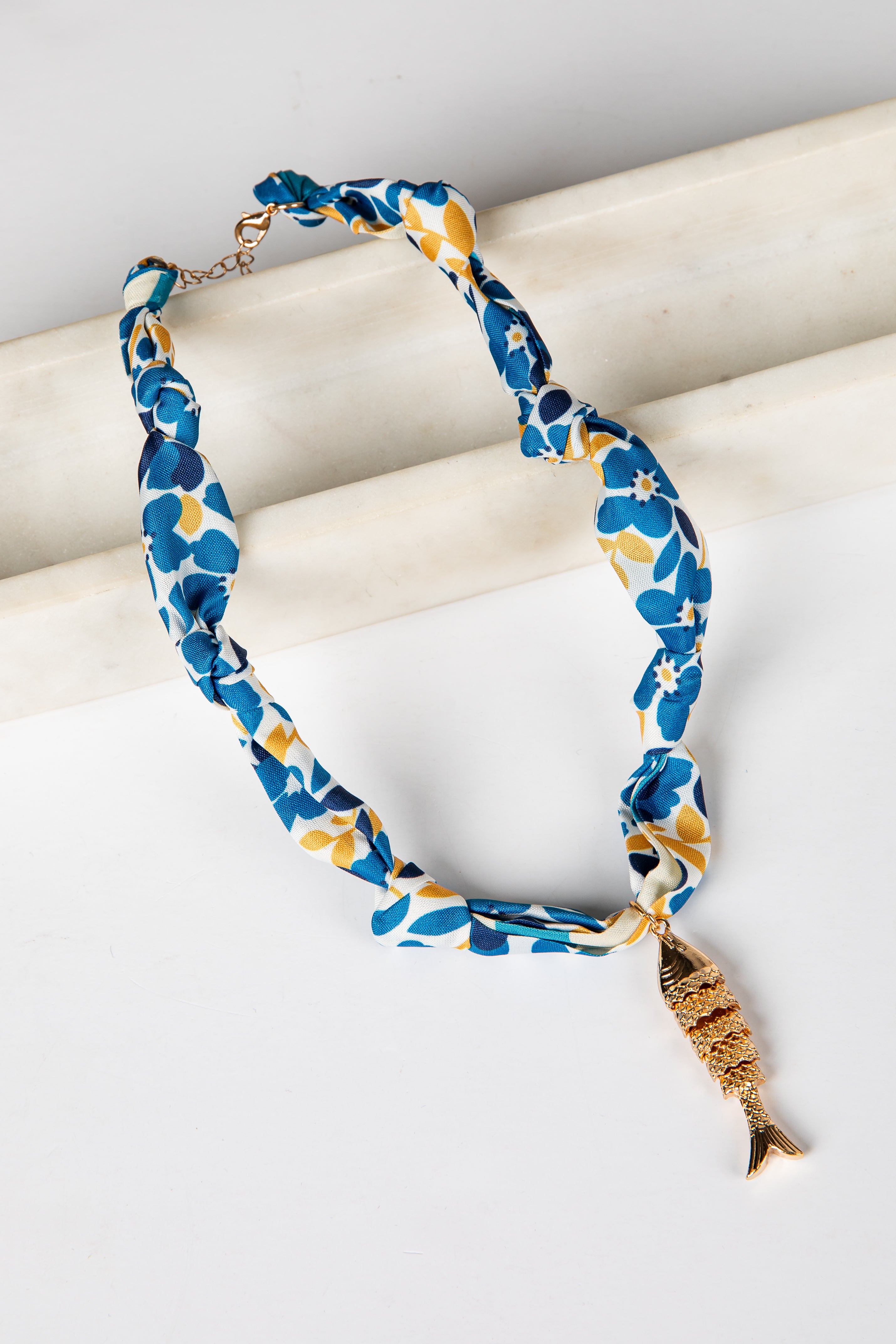 Blue and yellow floral-patterned necklace with a gold fish charm on a white background