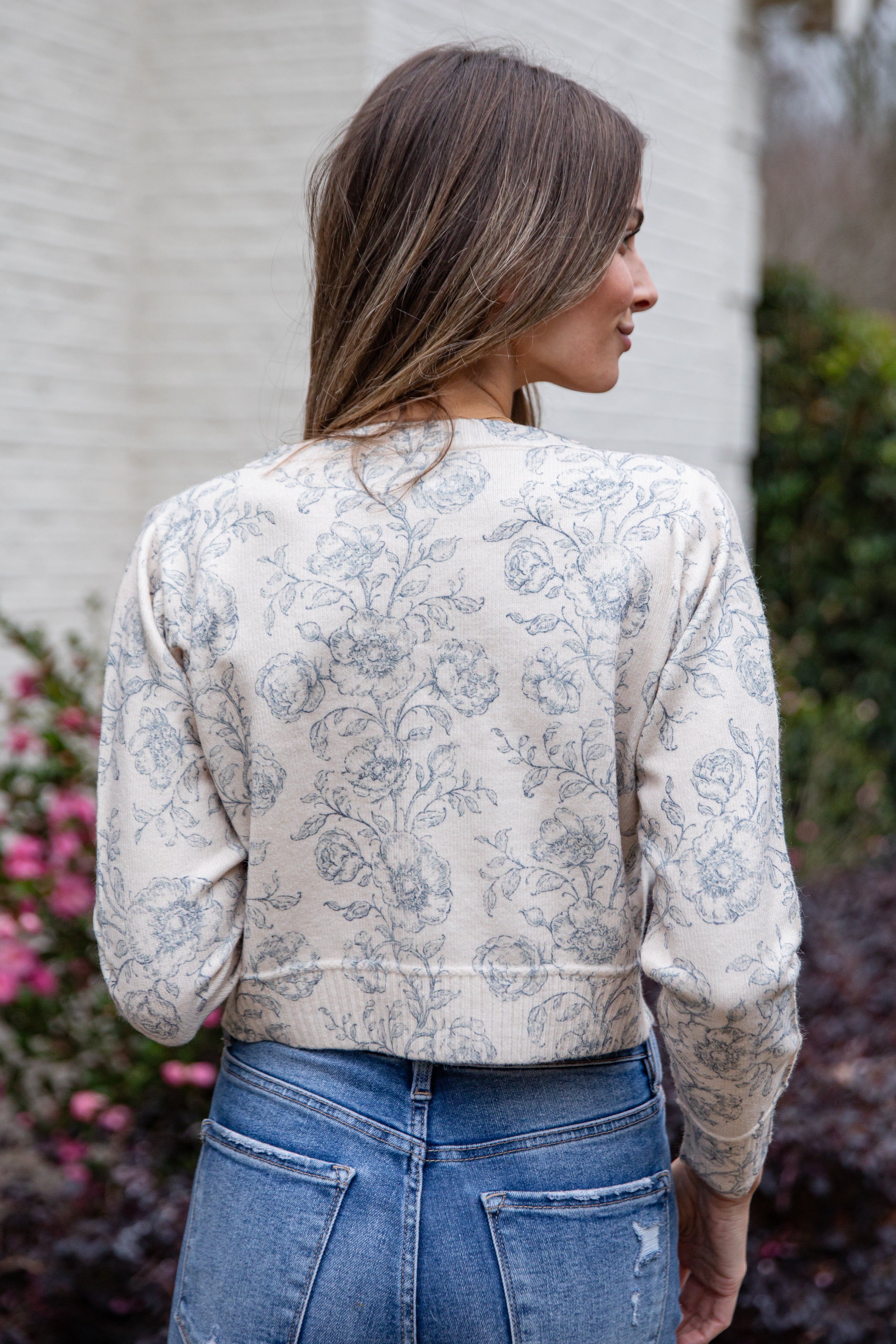Woman wearing a floral blouse and blue jeans outdoors.
