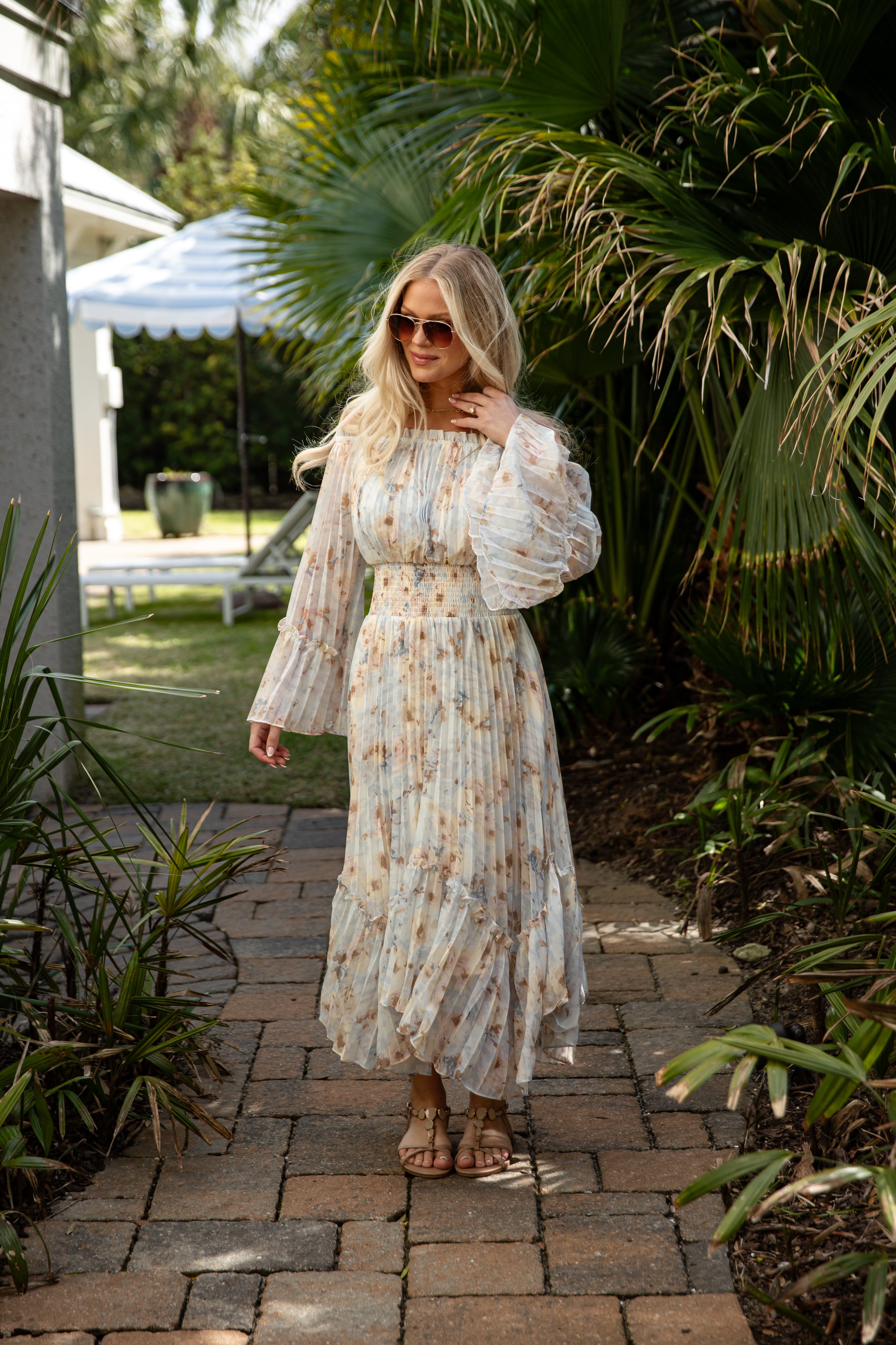 Woman in a floral dress standing on a paved path with greenery around