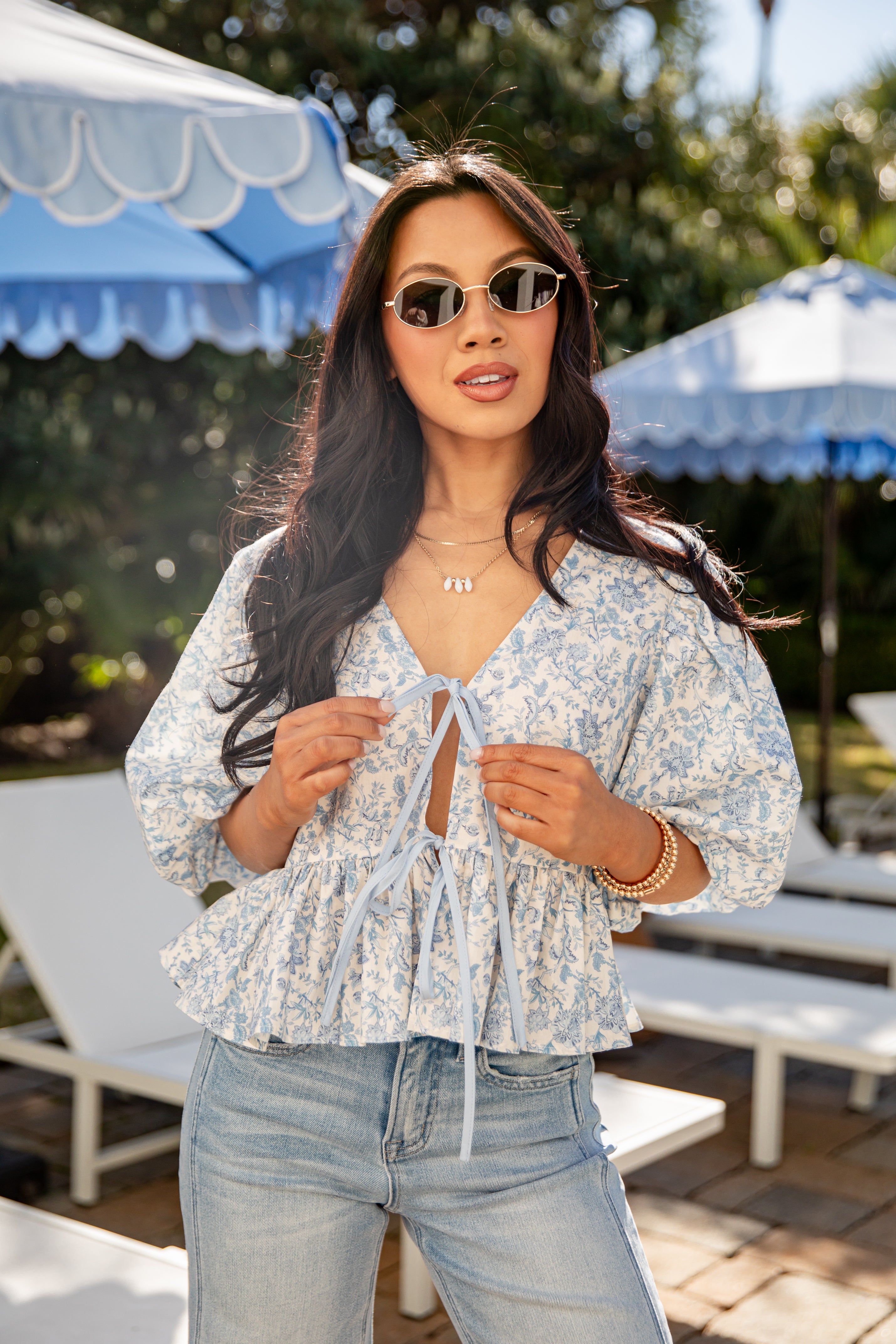 Woman wearing a floral blouse and sunglasses in an outdoor setting with blue umbrellas.