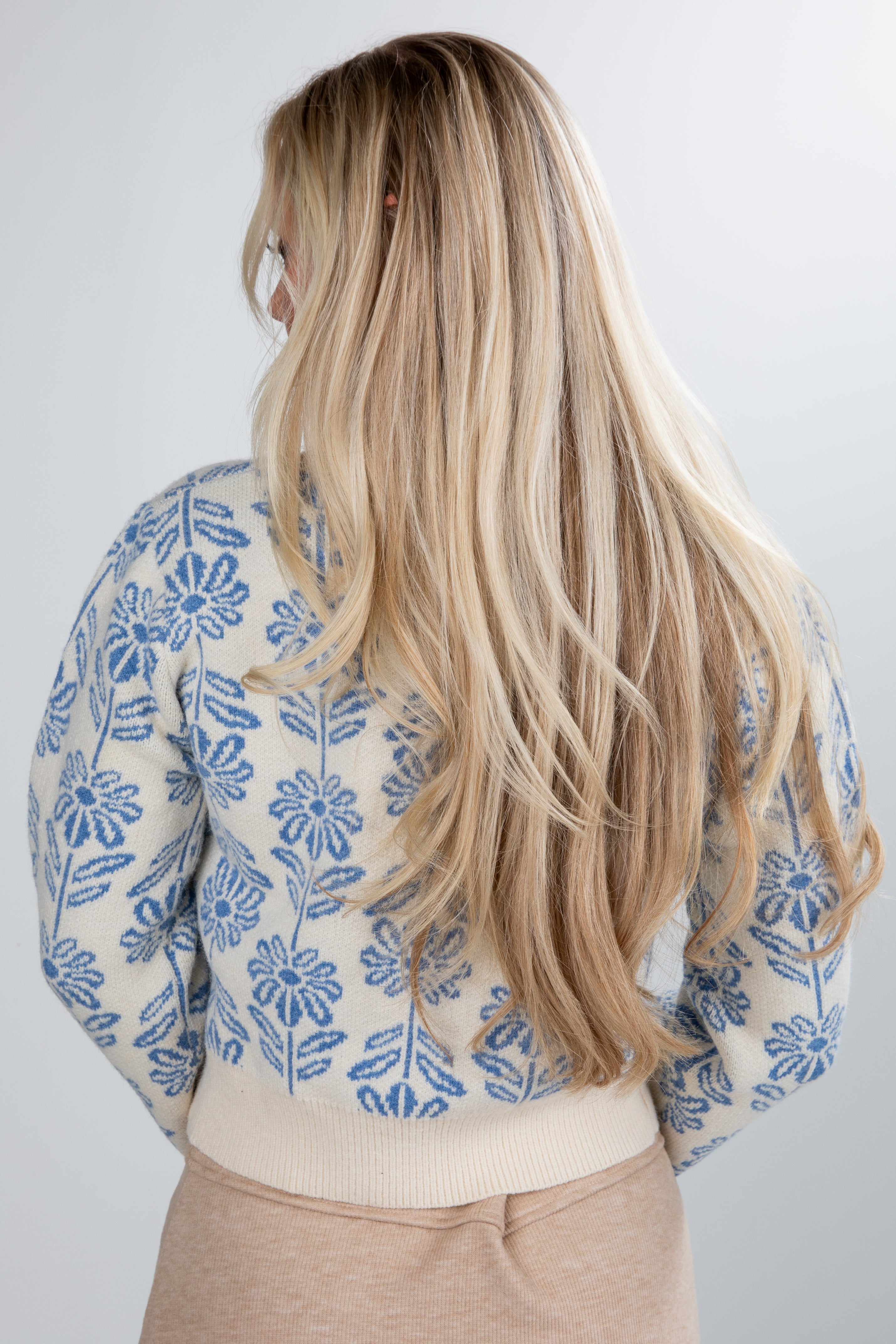 Person wearing a floral-patterned shirt with long blonde hair on a plain background