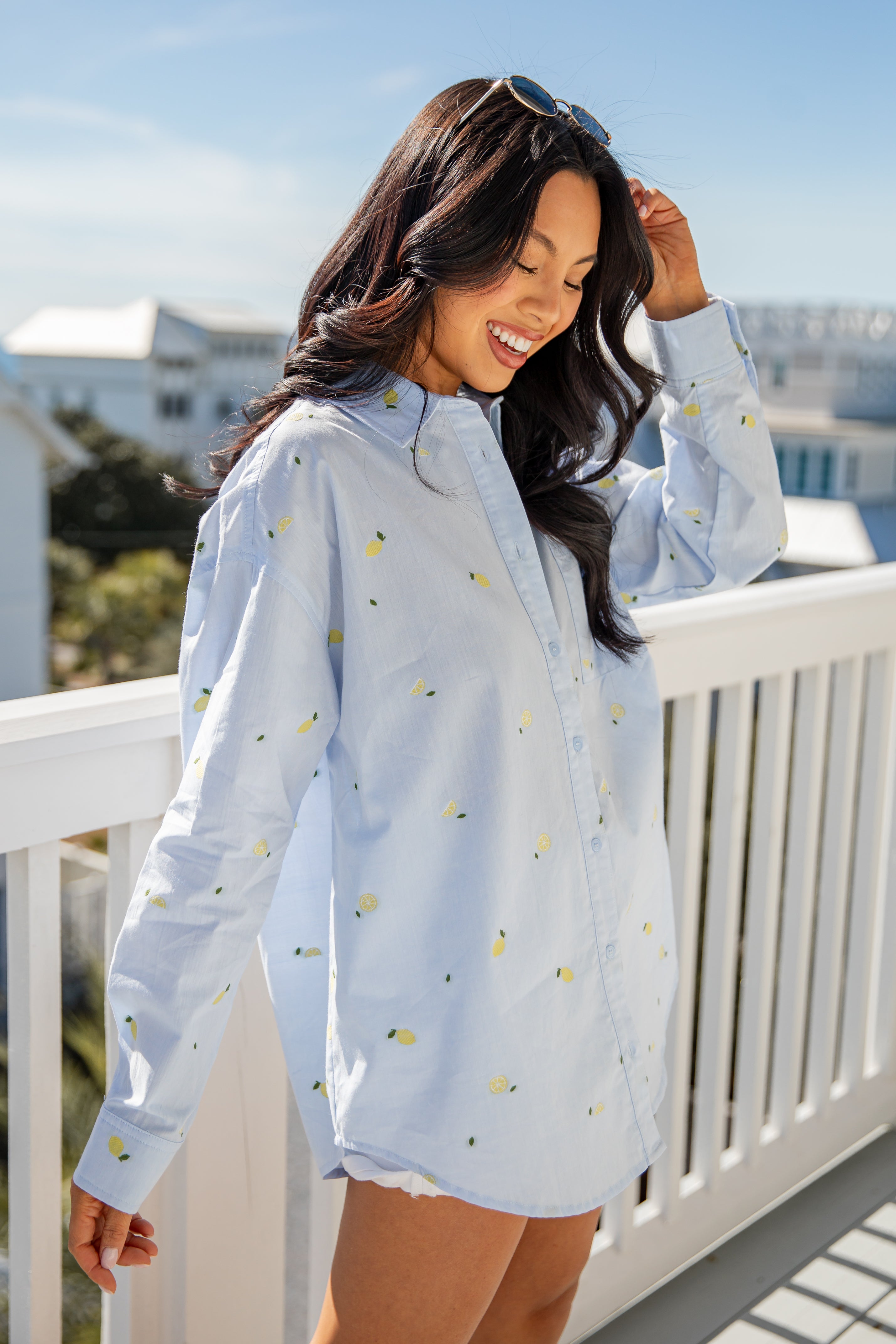 Woman wearing a light blue shirt with small patterns on a balcony with a scenic background