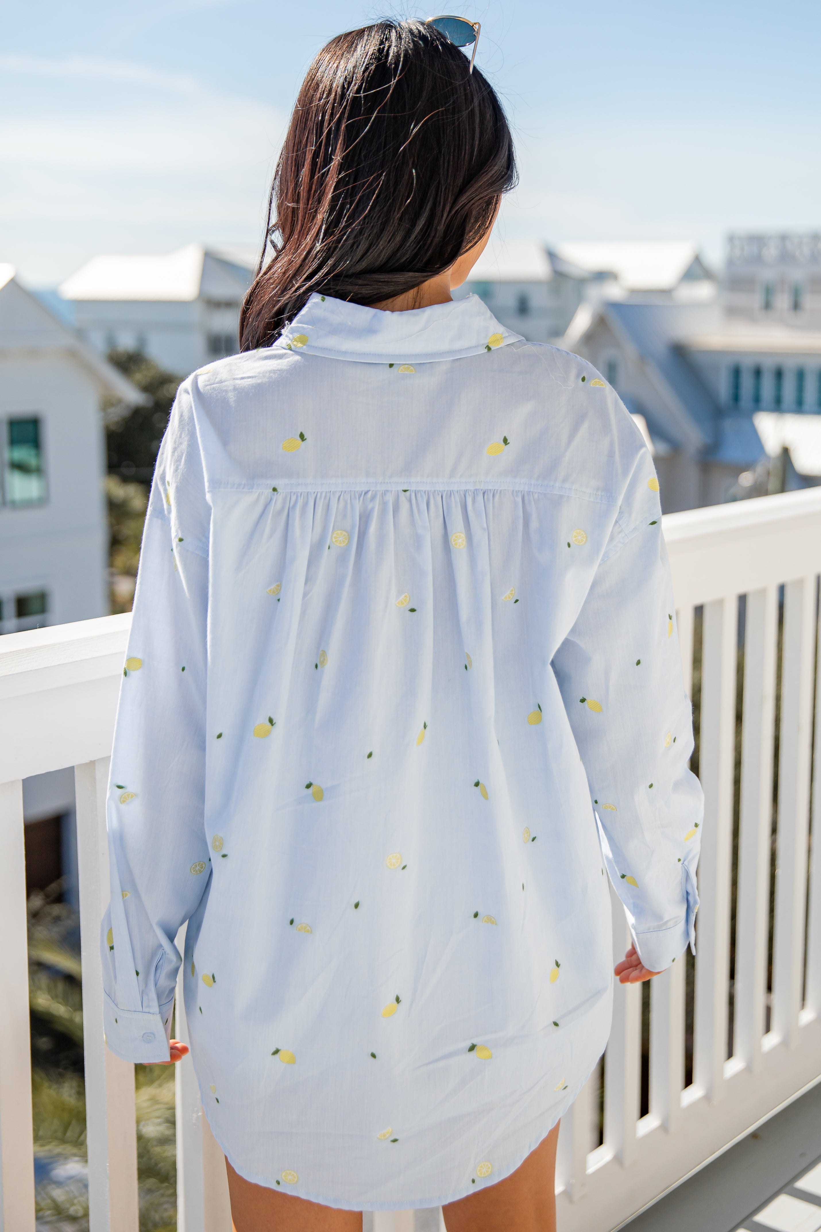 Woman wearing a light blue floral shirt on a balcony with a cityscape background