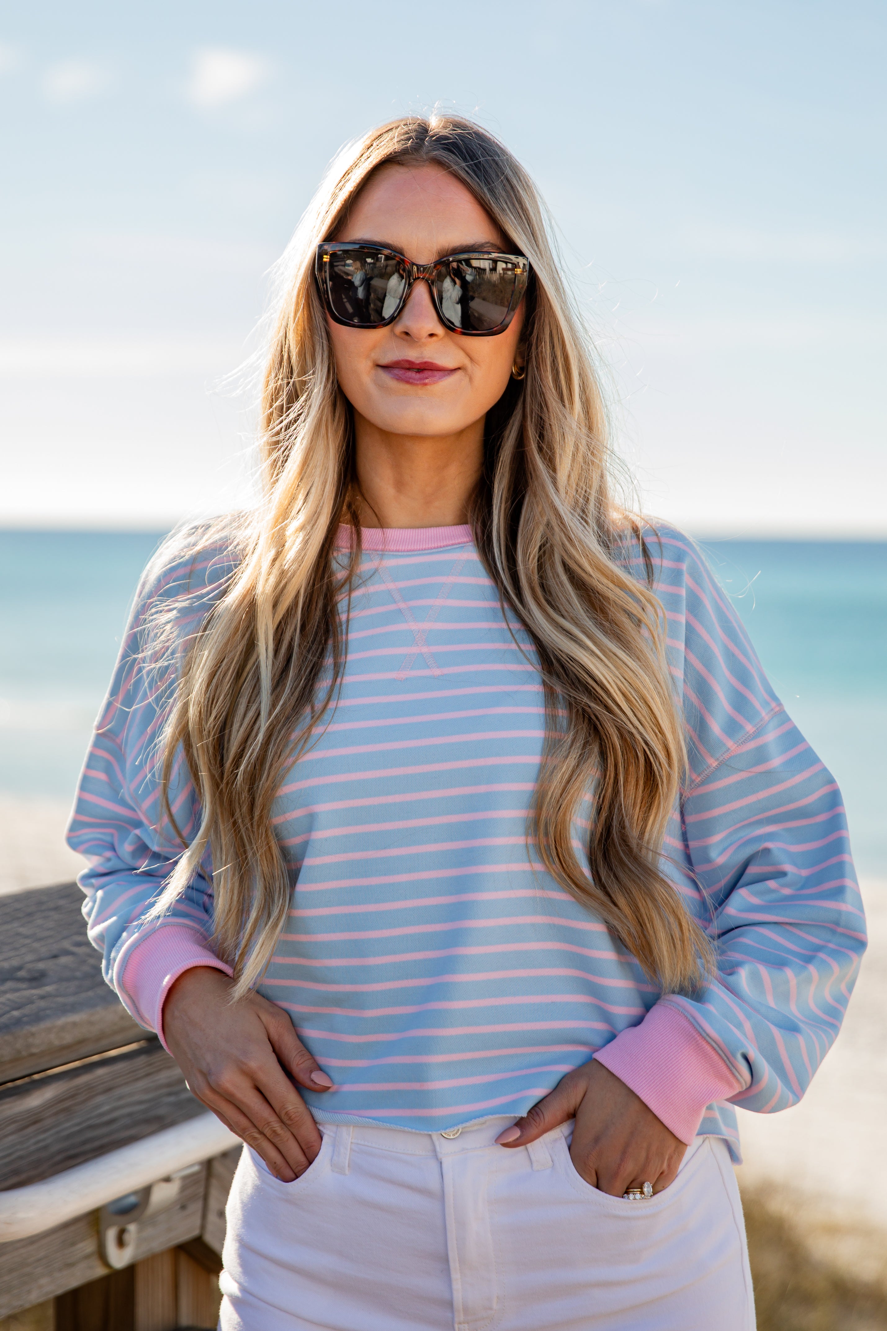 Woman wearing a striped shirt and sunglasses with a beach in the background