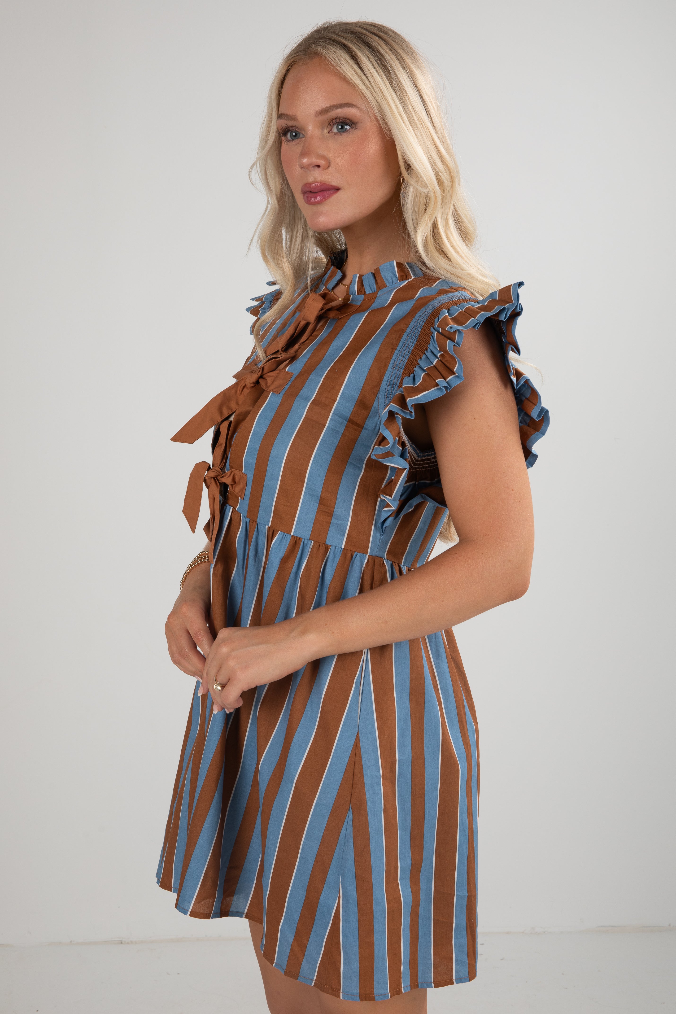 Woman wearing a brown and blue striped dress with ruffled sleeves against a white background