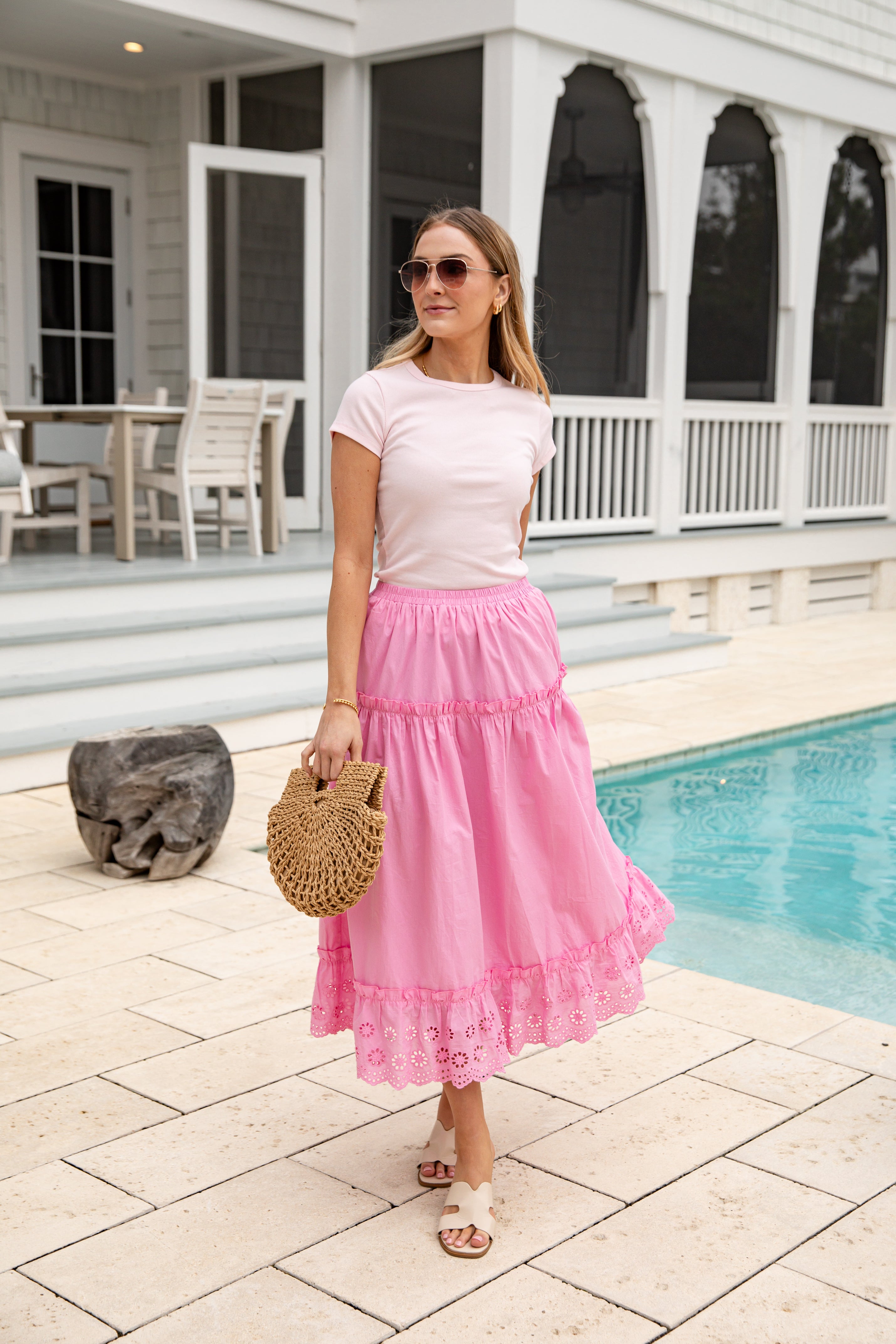 Woman in pink skirt and white top standing by a poolside.