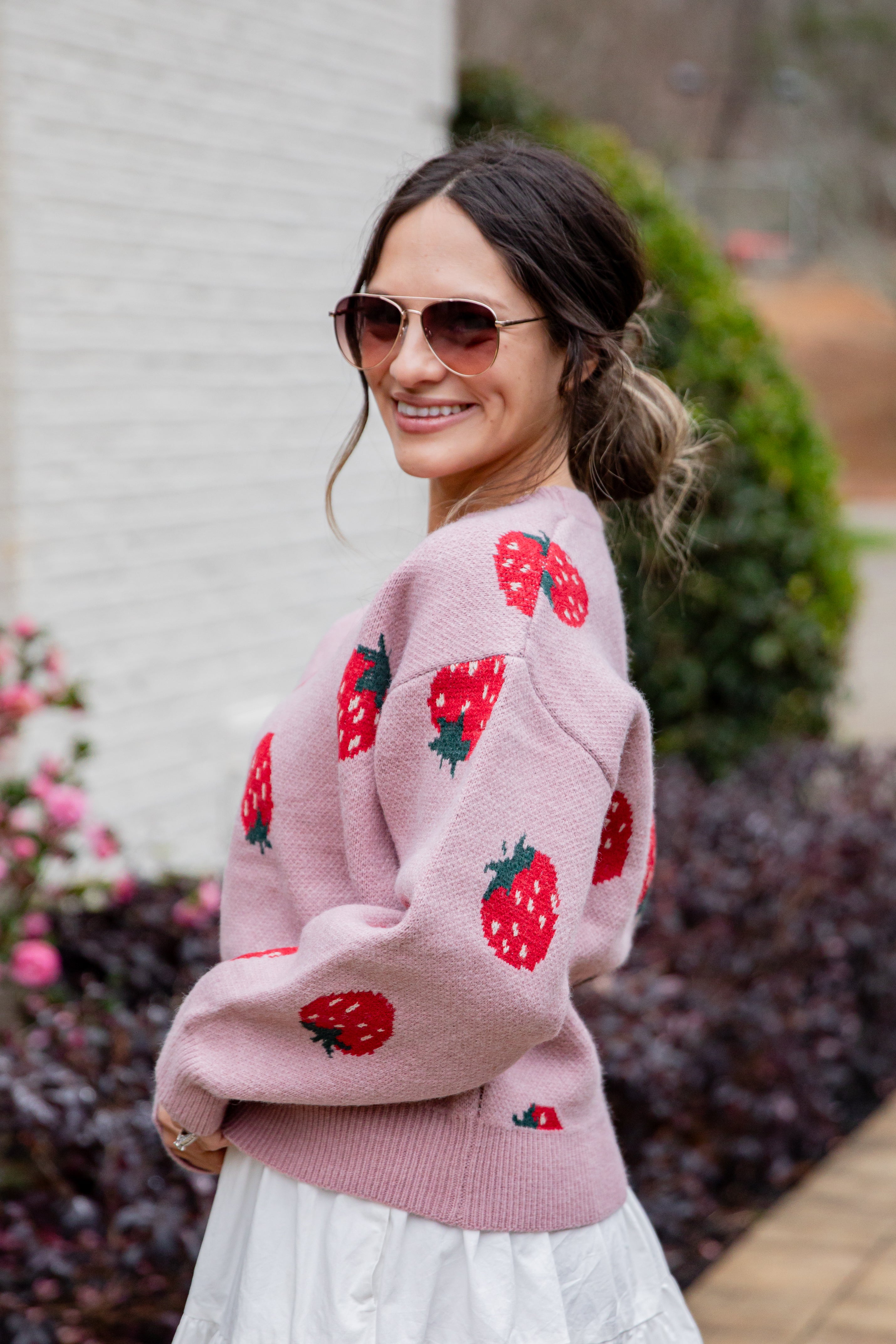 Woman wearing a pink sweater with strawberry patterns outdoors.