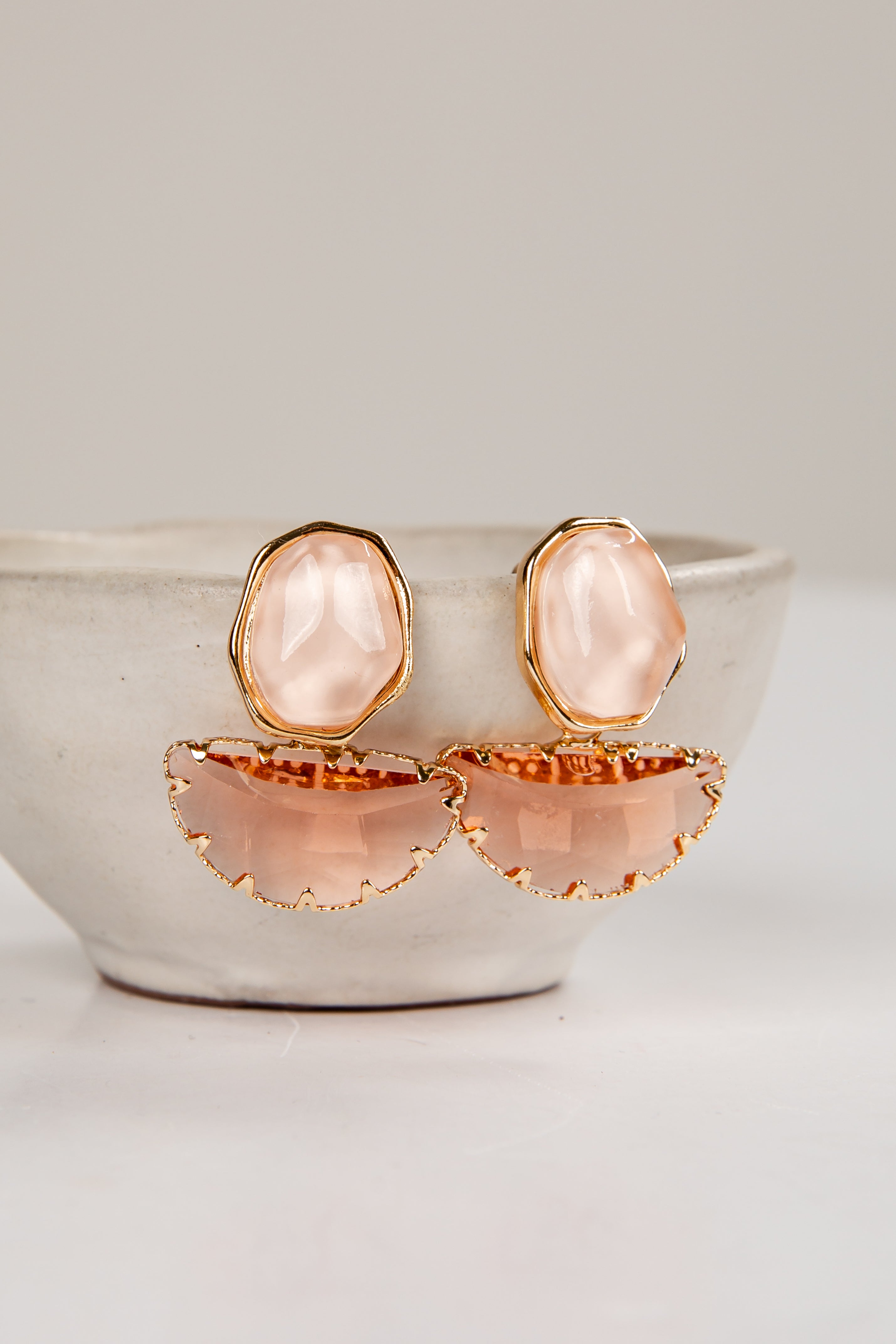 Pair of earrings with pink stones and gold accents on a white surface.