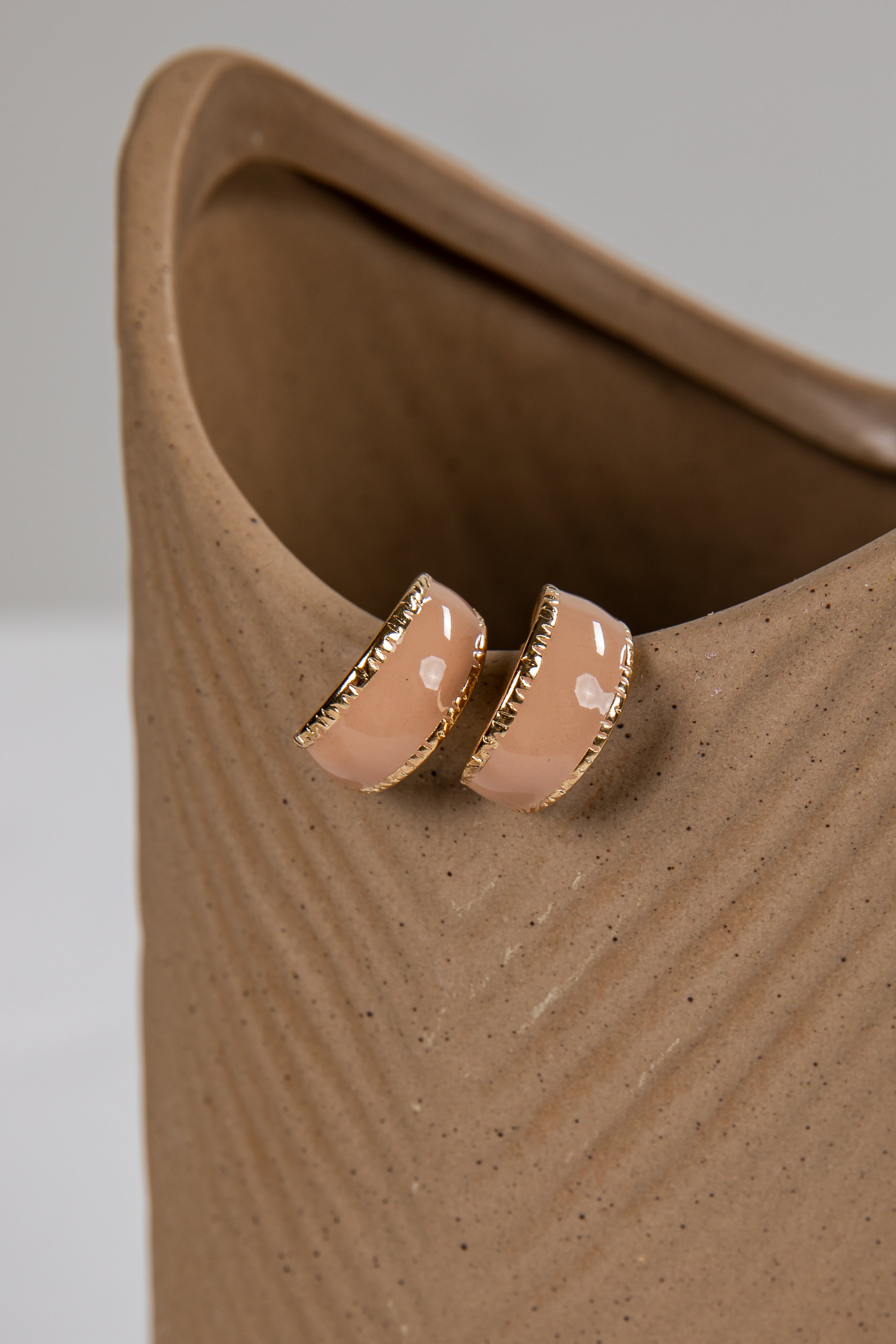 Pair of beige earrings with gold accents on a textured beige surface