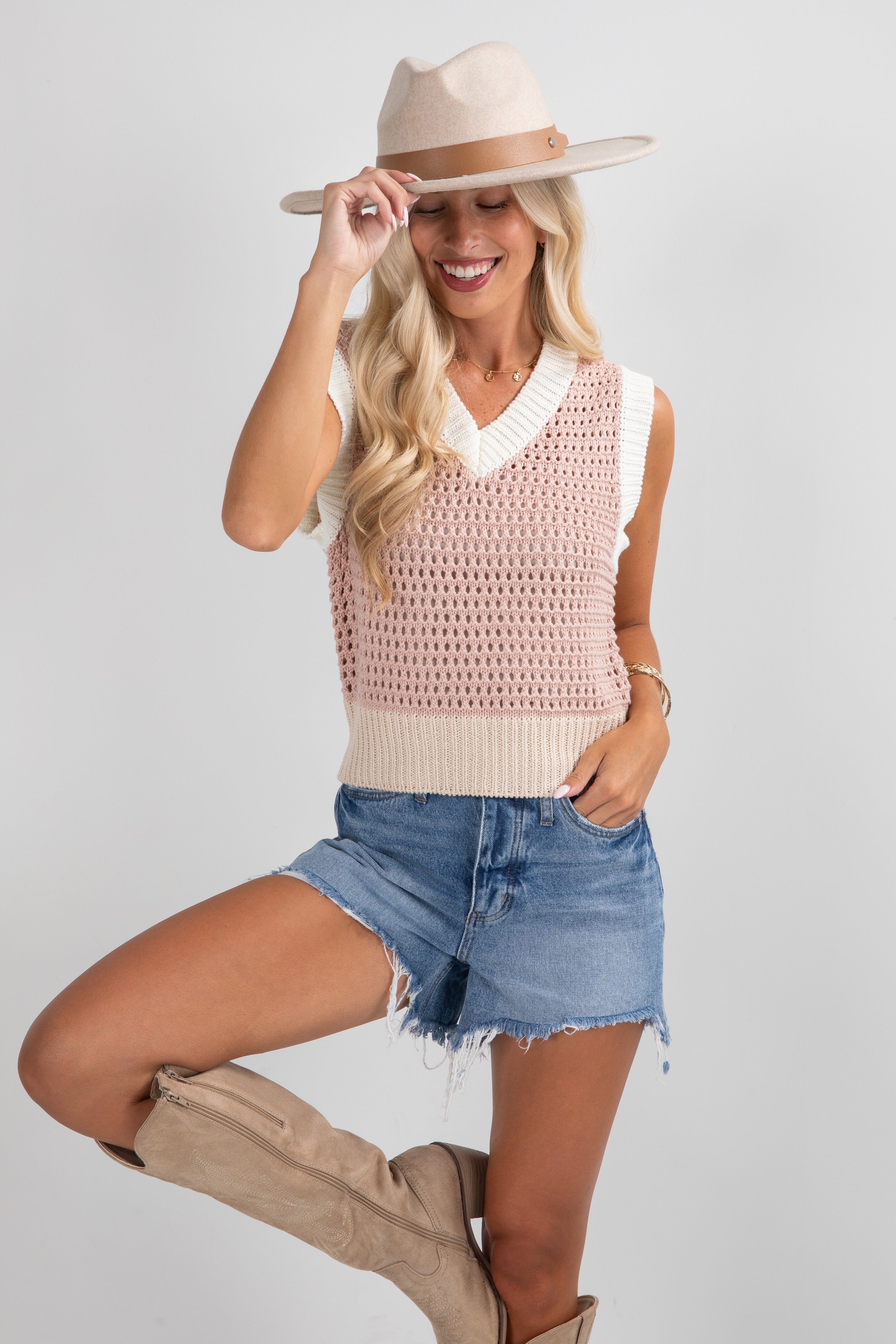 Woman wearing a sleeveless crochet top, denim shorts, and beige boots on a plain background